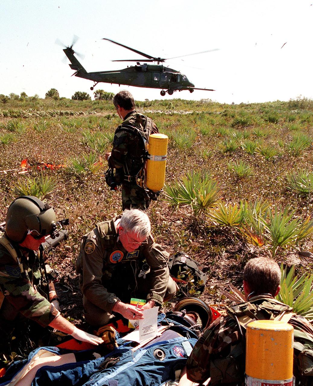 KENNEDY SPACE CENTER, FLA. -- During a simulated rescue mission in the woods near the Shuttle Landing Facility (SLF), the KSC response team practices stabilizing an injured crew member before transport to a local hospital by an Air Force HH-60 helicopter. The response team is training for the unlikely scenario of a Shuttle mishap at the SLF. The Mode 7 simulation of an astronaut rescue exercises all aspects of command and control, search and rescue, and medical procedures required for a successful rescue. The remote location of the mock-up prevents a totally land-based crew rescue, and calls on a NASA UH-1 helicopter to locate the site and four HH-60 helicopters to drop emergency equipment and fire/rescue workers to prepare the "crew" for preliminary triage. The helicopters are then used to remove the crew five astronaut candidates, one representative from the Vehicle Integration Test office, and one fire/rescue worker. The exercise will conclude with airlifted "patients" arriving safely in the emergency rooms of participating area hospitals