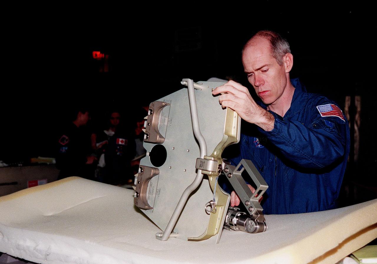 In the Orbiter Processing Facility bay 1, STS-96 Mission Specialist Daniel Barry, M.D., Ph.D., looks at one of the foot restraints used for extravehicular activity, or space walks. The STS-96 crew is at KSC to take part in a Crew Equipment Interface Test. The other crew members are Commander Kent V. Rominger, Pilot Rick Douglas Husband, and Mission Specialists Ellen Ochoa (Ph.D.), Tamara E. Jernigan (Ph.D.), Julie Payette and Valery Ivanovich Tokarev. Payette represents the Canadian Space Agency and Tokarev the Russian Space Agency. The primary payload of STS-96 is the SPACEHAB Double Module. In addition, the Space Shuttle will carry unpressurized cargo such as the external Russian cargo crane known as STRELA; the Spacehab Oceaneering Space System Box (SHOSS), which is a logistics items carrier; and an ORU Transfer Device (OTD), a U.S.-built crane that will be stowed on the station for use during future ISS assembly missions. These cargo items will be stowed on the International Cargo Carrier, fitted inside the payload bay behind the SPACEHAB module. STS-96 is targeted for launch on May 24 from Launch Pad 39B