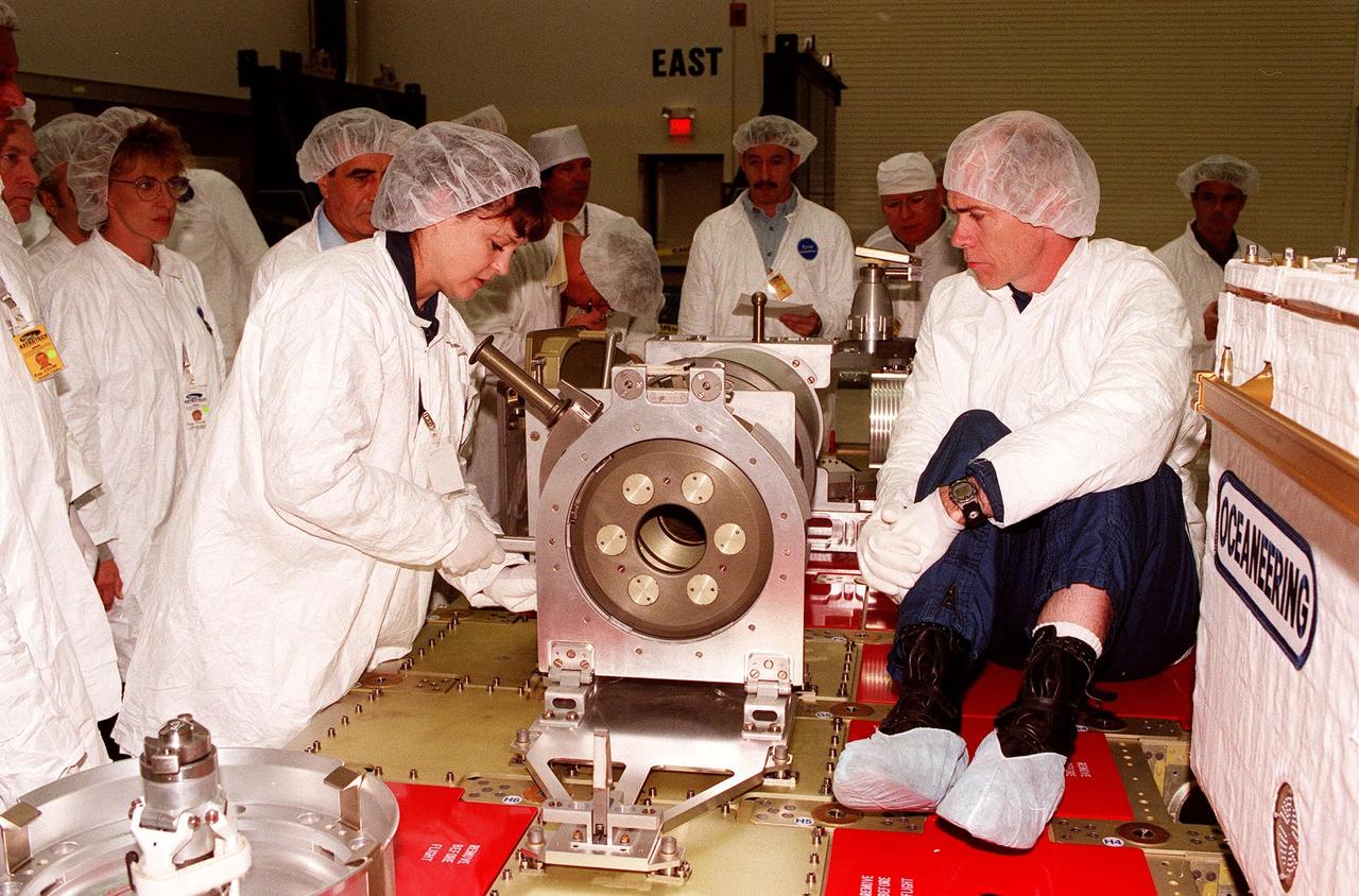 At Astrotech in Titusville, Fla., STS-96 Mission Specialists Tamara E. Jernigan and Daniel T. Barry take turns working with a Russian cargo crane, the Strela, which is to be mounted to the exterior of the Russian station segment on the International Space Station (ISS). Technicians around the table observe. The STS-96 crew is taking part in a Crew Equipment Interface Test. Other members participating are Commander Kent V. Rominger, Pilot Rick Douglas Husband, and Mission Specialists Julie Payette, with the Canadian Space Agency, and Valery Ivanovich Tokarev, with the Russian Space Agency. For the first time, STS-96 will include an Integrated Cargo Carrier (ICC) that will carry the Russian cargo crane; the SPACEHAB Oceaneering Space System Box (SHOSS), which is a logistics items carrier; and a U.S.-built crane (ORU Transfer Device, or OTD) that will be stowed on the station for use during future ISS assembly missions. The ICC can carry up to 6,000 lb of unpressurized payload. It was built for SPACEHAB by DaimlerChrysler Aerospace and RSC Energia of Korolev, Russia. STS-96 is targeted for launch on May 24 from Launch Pad 39B. STS-101 is scheduled to launch in early December 1999