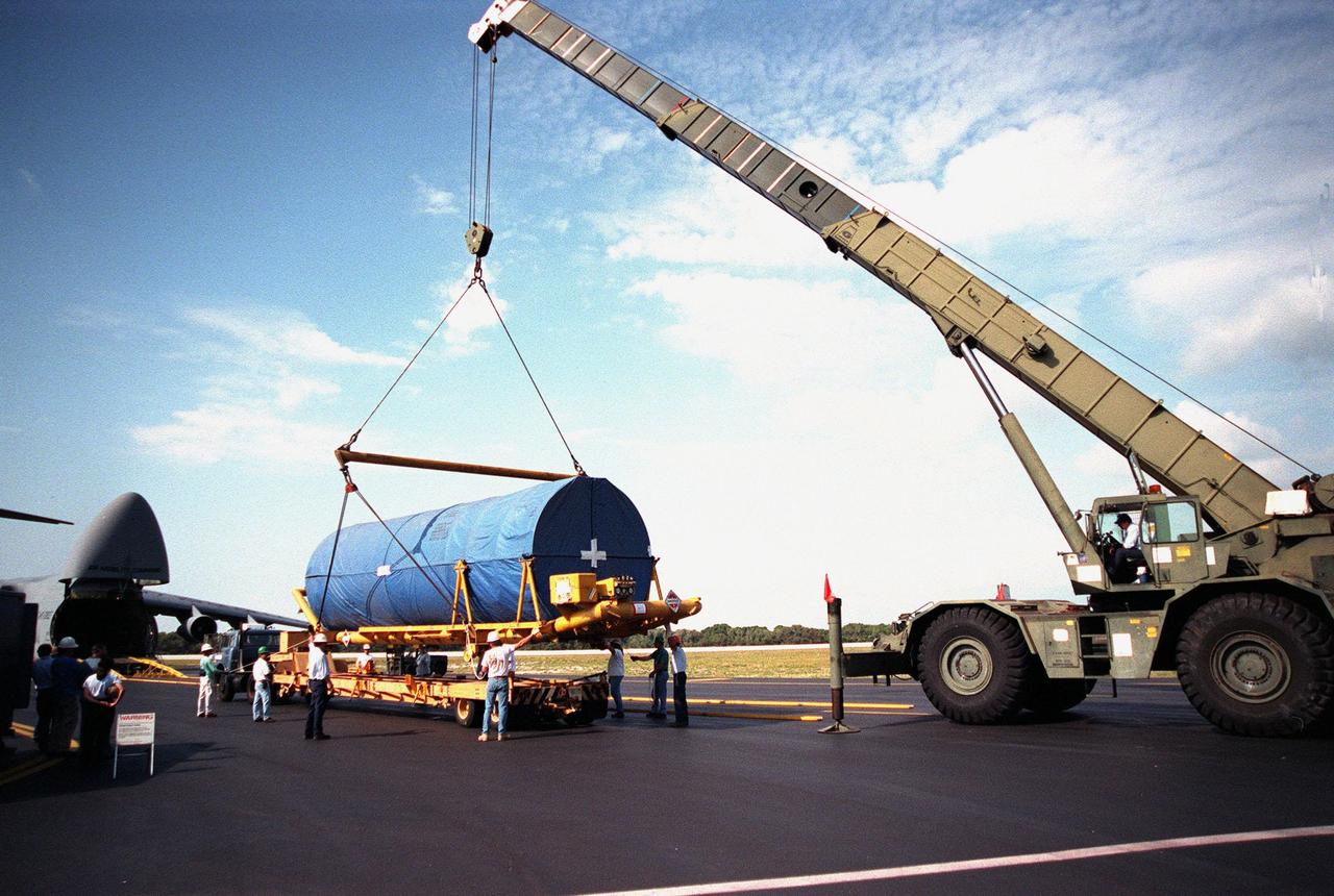 At Cape Canaveral Air Station (CCAS), workers help guide the crane lifting a Centaur upper stage onto a transporter. The Centaur arrived at CCAS aboard a U.S. Air Force C-5c (far left). After being mated with the Atlas IIA lower stage, the rocket is scheduled to launch the NASA GOES-L satellite from Launch Pad 36A on May 15. Once in orbit, the satellite will become GOES-11, joining GOES-8, GOES-9 and GOES-10 in space. The fourth of a new advanced series of geostationary weather satellites for the National Oceanic and Atmospheric Administration (NOAA), GOES-L is a three-axis inertially stabilized spacecraft that will provide pictures and perform atmospheric sounding at the same time. Once launched, the satellite will undergo checkout and then provide backup capabilities for the existing, aging operational satellites