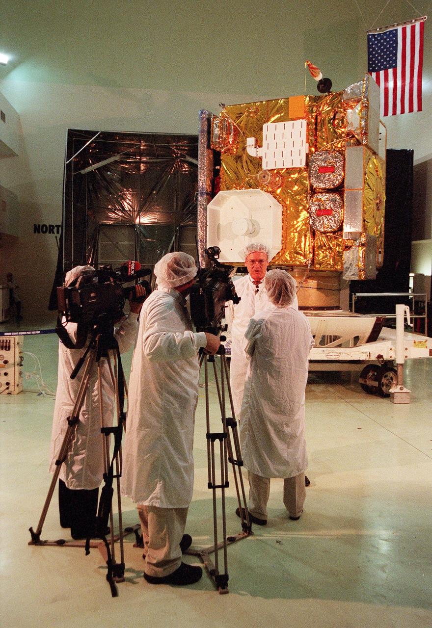 At Astrotech, in Titusville, Fla., GOES-L Program Manager Gerald Dittberner, with the National Oceanic and Atmospheric Administration (NOAA) talks with a journalist during a media showing of the GOES-L satellite in the background. The GOES-L is due to be launched May 15 from Launch Pad 36A aboard an Atlas IIA rocket. Once in orbit, the satellite will become GOES-11, joining GOES-8, GOES-9 and GOES-10 in space. The fourth of a new advanced series of geostationary weather satellites for the National Oceanic and Atmospheric Administration (NOAA), GOES-L is a three-axis inertially stabilized spacecraft that will provide pictures and perform atmospheric sounding at the same time. Once launched, the satellite will undergo checkout and then provide backup capabilities for the existing, aging operational satellites