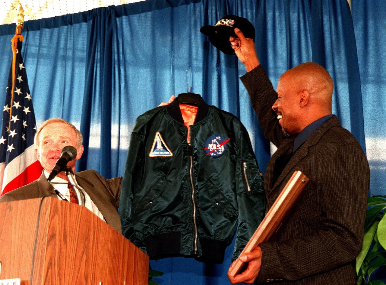 KENNEDY SPACE CENTER, FLA. -- At the grand opening of the newly expanded KSC Visitor Complex, Center Director Roy Bridges presents Deep Space Nine star Avery Brooks with a plaque, NASA jacket and hat. Brooks narrates the new film Quest for Life at the Visitor Center. Brooks was recognized for his contribution to advancing the public's understanding of NASA and the search for life elsewhere in the universe. The Complex now includes an International Space Station-themed ticket plaza, featuring a structure of overhanging solar panels and astronauts performing assembly tasks, a new foyer, films, and exhibits. The KSC Visitor Complex was inaugurated three decades ago and is now one of the top five tourist attractions in Florida. It is located on S.R. 407, east of I-95, within the Merritt Island National Wildlife Refuge