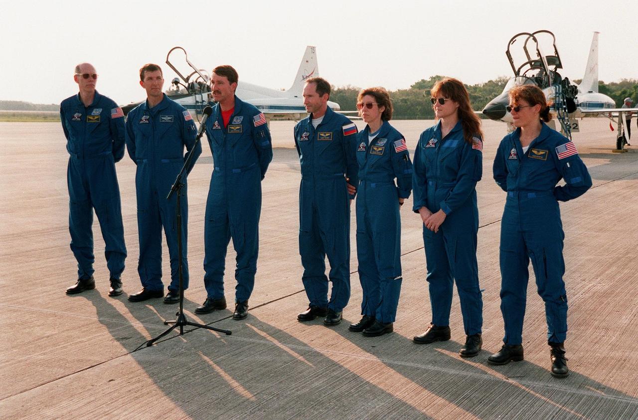 After arriving at Kennedy on the T-38 jet aircraft in the background, the STS-96 crew take a few minutes to talk to the media at the Shuttle Landing Facility. At the microphone is Commander Kent V. Rominger. With him are (left to right) Mission Specialist Daniel Barry (M.D., Ph.D.), Pilot Rick Douglas Husband, and Mission Specialists Valery Ivanovich Tokarev, Ellen Ochoa (Ph.D.), Tamara E. Jernigan (Ph.D.), and Julie Payette. Tokarev is with the Russian Space Agency and Payette is with the Canadian Space Agency. The crew are taking part in Terminal Countdown Demonstration Test (TCDT) activities. The TCDT provides simulated countdown exercises, emergency egress training, and opportunities to inspect the mission payloads in the orbiter's payload bay. Mission STS-96, which is targeted for launch on May 20 at 9:32 a.m., is a logistics and resupply mission for the International Space Station, carrying such payloads as a Russian crane, the Strela; a U.S.-built crane; the Spacehab Oceaneering Space System Box (SHOSS), a logistics items carrier; and STARSHINE, a student-led experiment