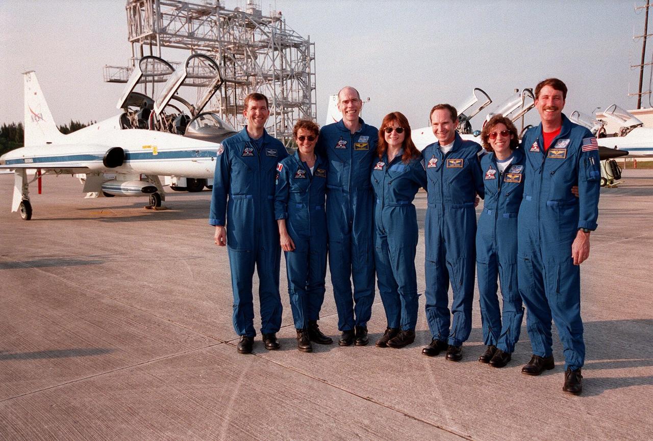 After arriving at Kennedy on the T-38 jet aircraft in the background, the STS-96 crew pose for photographers at the Shuttle Landing Facility. From left are Pilot Rick Douglas Husband; Mission Specialists Julie Payette, Daniel Barry (M.D., Ph.D.), Tamara E. Jernigan (Ph.D.), Valery Ivanovich Tokarev, and Ellen Ochoa (Ph.D.); and Commander Kent V. Rominger. Tokarev is with the Russian Space Agency and Payette is with the Canadian Space Agency. The crew are taking part in Terminal Countdown Demonstration Test (TCDT) activities. The TCDT provides simulated countdown exercises, emergency egress training, and opportunities to inspect the mission payloads in the orbiter's payload bay. Mission STS-96, which is targeted for launch on May 20 at 9:32 a.m., is a logistics and resupply mission for the International Space Station, carrying such payloads as a Russian crane, the Strela; a U.S.-built crane; the Spacehab Oceaneering Space System Box (SHOSS), a logistics items carrier; and STARSHINE, a student-led experiment