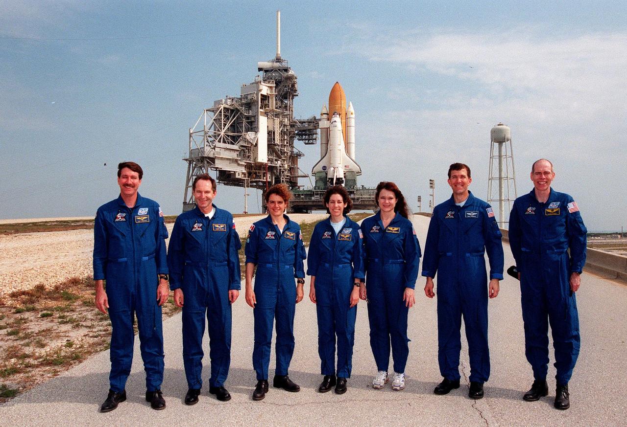 The STS-96 crew visit Launch Pad 39B where Space Shuttle Discovery, in the background, is being prepared for the mission launch on May 20. From left to right are Commander Kent V. Rominger; Mission Specialists Valery Ivanovich Tokarev, Julie Payette, Ellen Ochoa (Ph.D.), and Tamara E. Jernigan (Ph.D.); Pilot Rick Douglas Husband; and Mission Specialist Daniel Barry (M.D., Ph.D.). The crew are taking part in Terminal Countdown Demonstration Test (TCDT) activities. The TCDT provides simulated countdown exercises, emergency egress training, and opportunities to inspect the mission payloads in the orbiter's payload bay. Mission STS-96 is a logistics and resupply mission for the International Space Station, carrying such payloads as a Russian crane, the Strela; a U.S.-built crane; the Spacehab Oceaneering Space System Box (SHOSS), a logistics items carrier; and STARSHINE, a student-led experiment