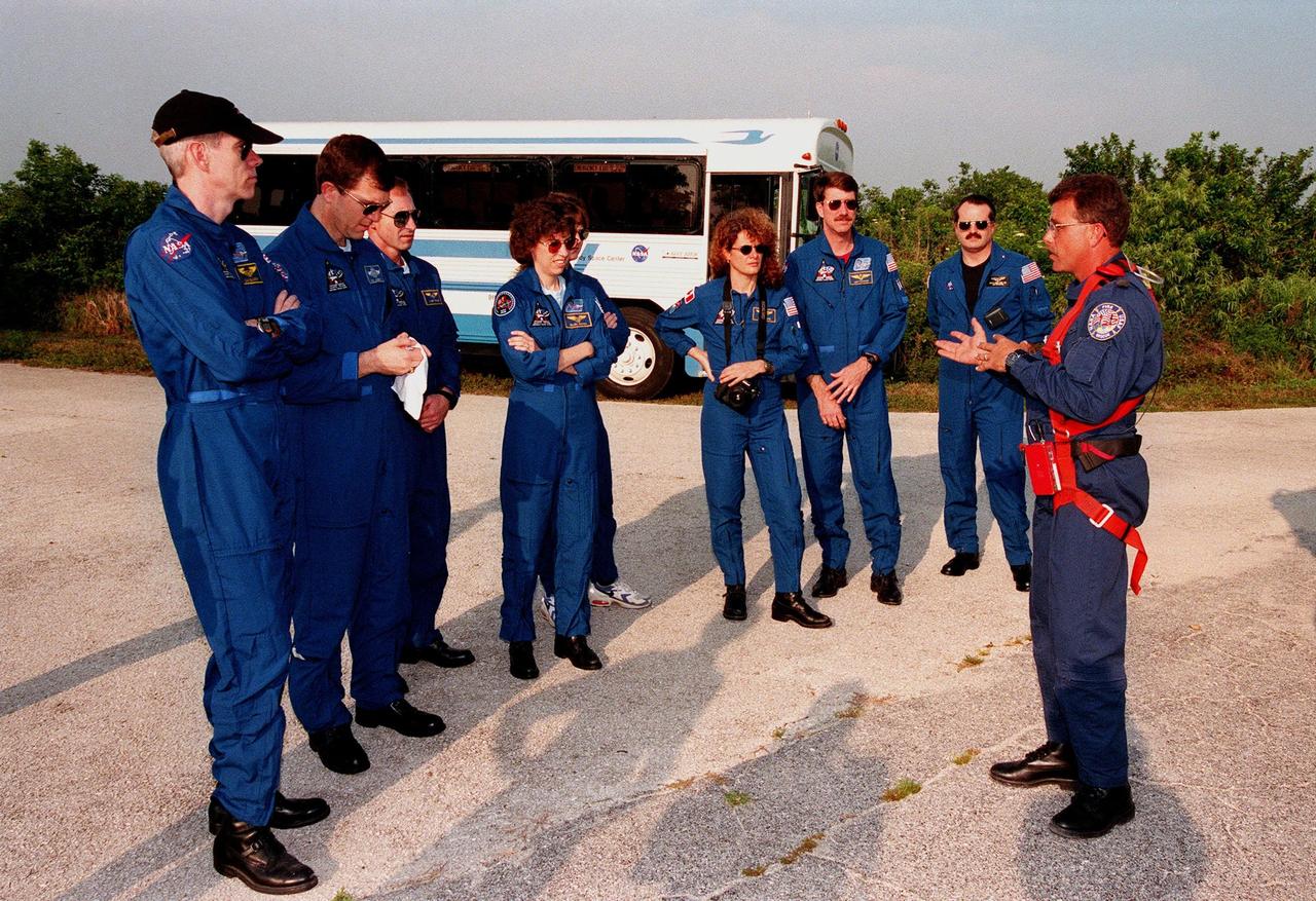The STS-96 crew listen to Capt. Steve Kelly, with Space Gateway Support, who is assisting with emergency egress training during Terminal Countdown Demonstration Test (TCDT) activities. The TCDT also provides simulated countdown exercises and opportunities to inspect the mission payloads in the orbiter's payload bay. From left are Mission Specialist Daniel Barry (M.D., Ph.D.), Pilot Rick Douglas Husband, Mission Specialists Valery Ivanovich Tokarev, Ellen Ochoa (Ph.D.), Tamara E. Jernigan (Ph.D.) and Julie Payette, and Commander Kent V. Rominger. Next to Rominger is Douglas Hamilton, Canadian flight surgeon. Payette is with the Canadian Space Agency. Tokarev represents the Russian Space Agency. Mission STS-96, which is scheduled for liftoff on May 20 at 9:32 a.m., is a logistics and resupply mission for the International Space Station, carrying such payloads as a Russian crane, the Strela; a U.S.-built crane; the Spacehab Oceaneering Space System Box (SHOSS), a logistics items carrier; and STARSHINE, a student-led experiment