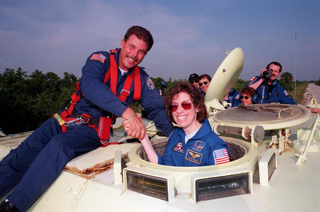 Capt. Steve Kelly, with Space Gateway Support, congratulates STS-96 Mission Specialist Ellen Ochoa (Ph.D.), who successfully completed training in the small armored personnel carrier that is part of emergency egress training during Terminal Countdown Demonstration Test (TCDT) activities. The tracked vehicle could be used by the crew in the event of an emergency at the pad during which the crew must make a quick exit from the area. Behind them (from left) are crew members Mission Specialist Valery Ivanovich Tokarev, Pilot Rick Douglas Husband and Mission Specialist Julie Payette. Holding the camera is Douglas Hamilton, a Canadian flight surgeon. Payette is with the Canadian Space Agency. Tokarev represents the Russian Space Agency. The TCDT also provides simulated countdown exercises and opportunities to inspect the mission payloads in the orbiter's payload bay. Mission STS-96, which is scheduled for liftoff on May 20 at 9:32 a.m., is a logistics and resupply mission for the International Space Station, carrying such payloads as a Russian crane, the Strela; a U.S.-built crane; the Spacehab Oceaneering Space System Box (SHOSS), a logistics items carrier; and STARSHINE, a student-led experiment