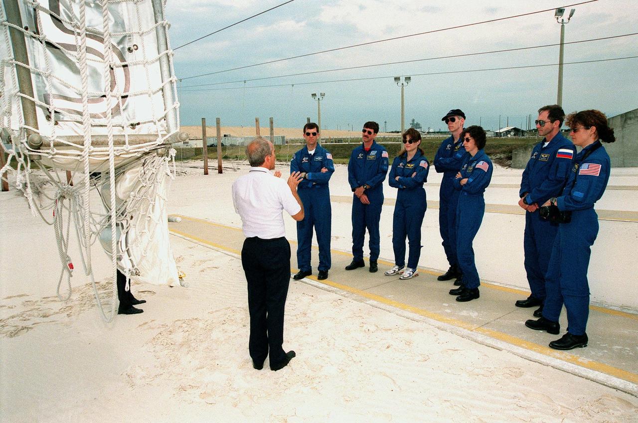 At Launch Pad 39B, the STS-96 crew listens to tech trainer Ken Clark, with United Space Alliance, about the use of the slidewire basket at left during emergency egress training. Standing left to right are Pilot Rick Douglas Husband, Commander Kent V. Rominger, and Mission Specialists Tamara E. Jernigan (Ph.D.), Daniel Barry (M.D., Ph.D.), Ellen Ochoa (Ph.D.), Valery Ivanovich Tokarev, with the Russian Space Agency, and Julie Payette, with the Canadian Space Agency. The STS-96 crew are taking part in Terminal Countdown Demonstration Test activities which also provide simulated countdown exercises and opportunities to inspect the mission payloads in the orbiter's payload bay. Scheduled for liftoff on May 20 at 9:32 a.m., STS-96 is a logistics and resupply mission for the International Space Station, carrying such payloads as a Russian crane, the Strela; a U.S.-built crane; the Spacehab Oceaneering Space System Box (SHOSS), a logistics items carrier; and STARSHINE, a student-led experiment