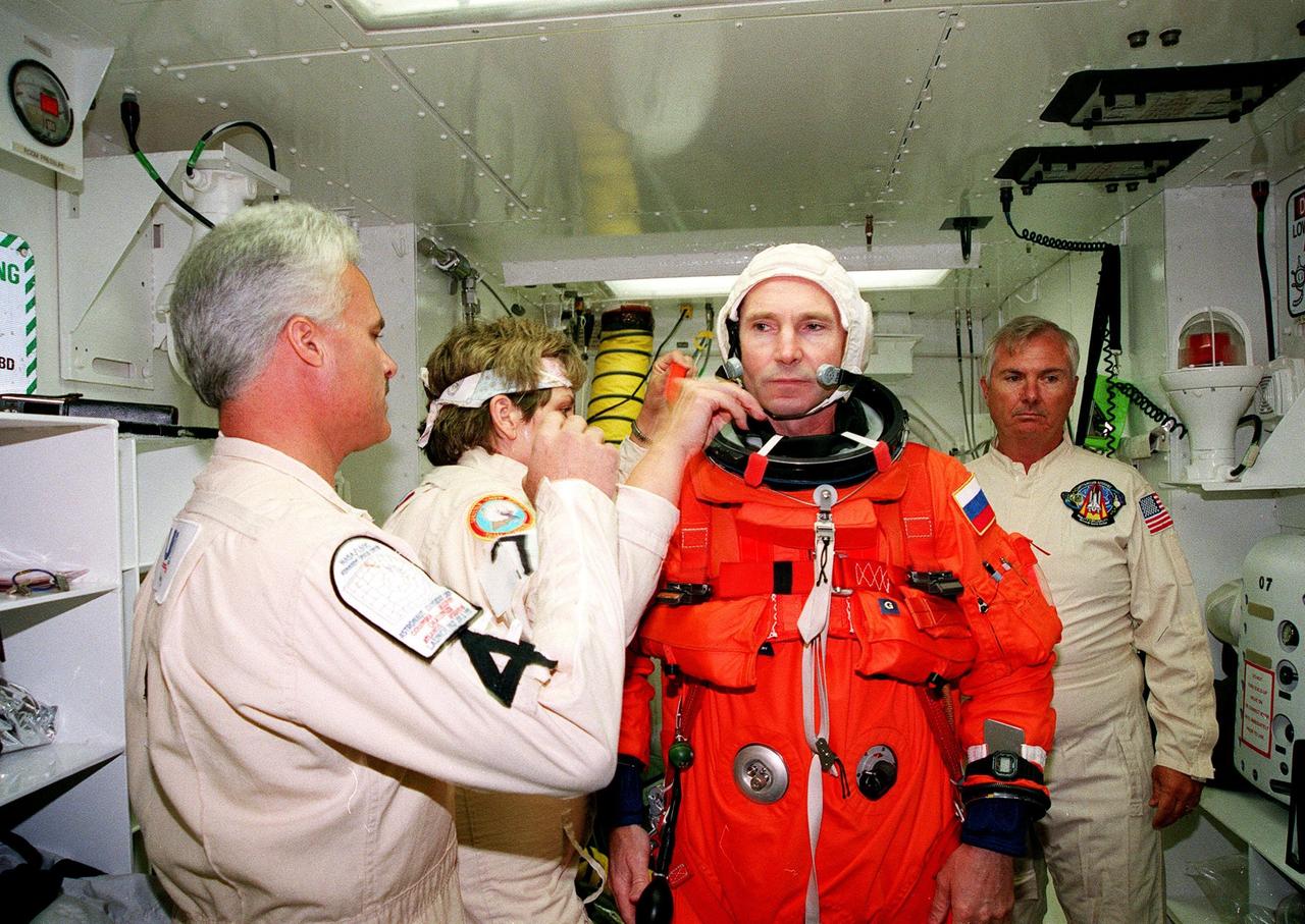 In the white room, an environmental chamber, at Launch Pad 39B, STS-96 Mission Specialist Valery Ivanovich Tokarev, with the Russian Space Agency, gets help with equipment from Chris Menard, Jean Alexander and James Davis before entering the orbiter Discovery at Launch Pad 39B. The crew are taking part in Terminal Countdown Demonstration Test (TCDT) activities, which provide opportunities to inspect the mission payloads in the orbiter's payload bay, as well as simulated countdown exercises and emergency egress training. STS-96, scheduled for liftoff on May 20 at 9:32 a.m., is a logistics and resupply mission for the International Space Station, carrying such payloads as a Russian crane, the Strela; a U.S.-built crane; the Spacehab Oceaneering Space System Box (SHOSS), a logistics items carrier; and STARSHINE, a student-led experiment