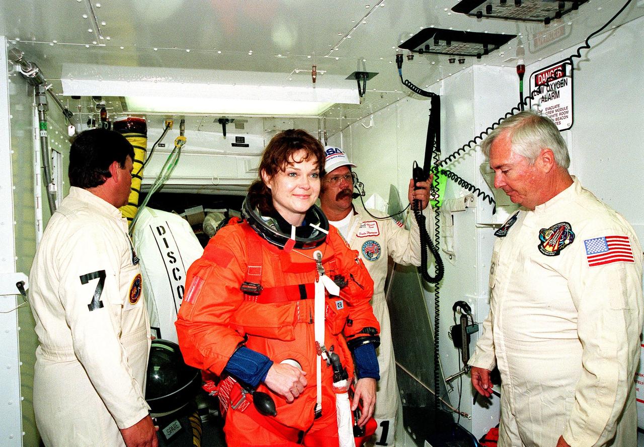 In the white room, an environmental chamber at Launch Pad 39B, Mission Specialist Tamara E. Jernigan (Ph.D.) gets ready to enter the orbiter Discovery. Helping her with her equipment are (left to right) Mike Birkenscher, Travis Thompson and James Davis. The STS-96 crew are taking part in Terminal Countdown Demonstration Test (TCDT) activities, which provide opportunities to inspect the mission payloads in the orbiter's payload bay, as well as simulated countdown exercises and emergency egress training. Other crew members are Commander Kent V. Rominger, Pilot Rick Douglas Husband, and Mission Specialists Ellen Ochoa (Ph.D.), Daniel Barry (M.D., Ph.D.), Julie Payette, who is with the Canadian Space Agency, and Valery Ivanovich Tokarev, who is with the Russian Space Agency. STS-96, scheduled for liftoff on May 20 at 9:32 a.m., is a logistics and resupply mission for the International Space Station, carrying such payloads as a Russian crane, the Strela; a U.S.-built crane; the Spacehab Oceaneering Space System Box (SHOSS), a logistics items carrier; and STARSHINE, a student-led experiment
