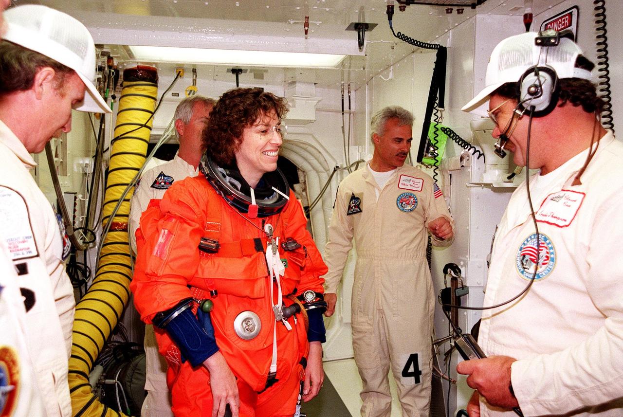 In the white room, an environmental chamber at Launch Pad 39B, Mission Specialist Ellen Ochoa (Ph.D.) gets help with her equipment from Al Schmidt, Chris Menard and Travis Thompson before she enters the orbiter Discovery. The STS-96 crew are taking part in Terminal Countdown Demonstration Test (TCDT) activities, which provide opportunities to inspect the mission payloads in the orbiter's payload bay, as well as simulated countdown exercises and emergency egress training. Other crew members are Commander Kent V. Rominger, Pilot Rick Douglas Husband, and Mission Specialists Tamara E. Jernigan (Ph.D.), Daniel Barry (M.D., Ph.D.), Julie Payette, who is with the Canadian Space Agency, and Valery Ivanovich Tokarev, who is with the Russian Space Agency. STS-96, scheduled for liftoff on May 20 at 9:32 a.m., is a logistics and resupply mission for the International Space Station, carrying such payloads as a Russian crane, the Strela; a U.S.-built crane; the Spacehab Oceaneering Space System Box (SHOSS), a logistics items carrier; and STARSHINE, a student-led experiment
