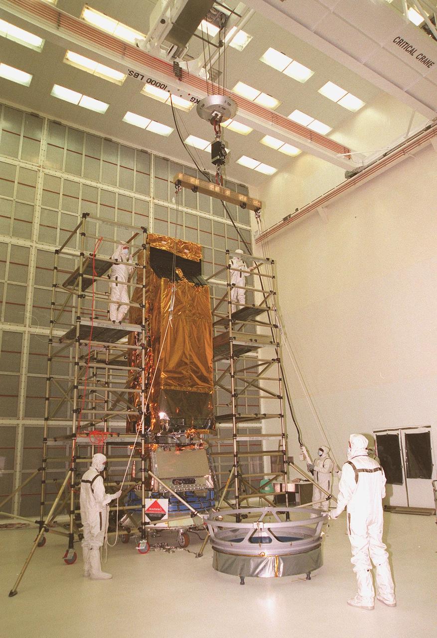 Workers at Hangar AE, Cape Canaveral Air Station, maneuver an overhead crane toward NASA's Far Ultraviolet Spectroscopic Explorer (FUSE) satellite standing between vertical workstands. The crane will lift FUSE to move it onto the Payload Attach Fitting (PAF) in front of it. FUSE is undergoing a functional test of its systems, plus installation of flight batteries and solar arrays. Developed by The Johns Hopkins University under contract to Goddard Space Flight Center, Greenbelt, Md., FUSE will investigate the origin and evolution of the lightest elements in the universe hydrogen and deuterium. In addition, the FUSE satellite will examine the forces and process involved in the evolution of the galaxies, stars and planetary systems by investigating light in the far ultraviolet portion of the electromagnetic spectrum. FUSE is scheduled to be launched May 27 aboard a Boeing Delta II rocket at Launch Complex 17