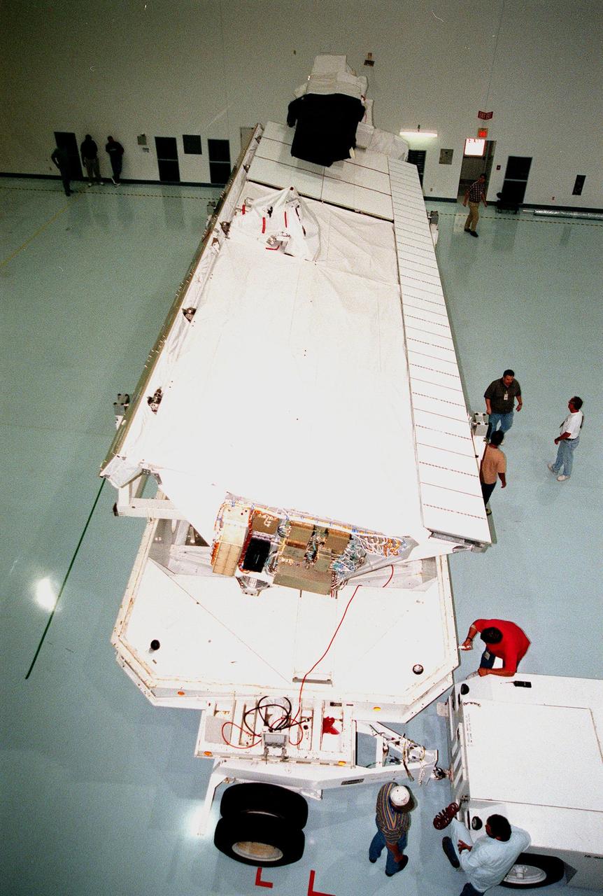 In the Space Station Processing Facility (SSPF), workers (lower right) disconnect the transport vehicle from the Shuttle Radar Topography Mission (SRTM) after moving it into the building for pre-launch preparations. The primary payload on mission STS-99, the SRTM consists of a specially modified radar system that will fly onboard the Space Shuttle during the 11-day mission targeted for launch in September 1999. This radar system will gather data that will result in the most accurate and complete topographic map of the Earth's surface that has ever been assembled. SRTM is an international project spearheaded by the National Imagery and Mapping Agency and NASA, with participation of the German Aerospace Center DLR. Its objective is to obtain the most complete high-resolution digital topographic database of the Earth