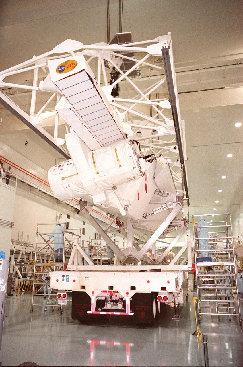 Workers inside the Space Station Processing Facility keep watch as an overhead crane begins lifting the Shuttle Radar Topography Mission (SRTM) from the transporter below. The SRTM is being moved to a workstand. The primary payload on mission STS-99, the SRTM consists of a specially modified radar system that will fly onboard the Space Shuttle during the 11-day mission scheduled for launch in September 1999. The objective of this radar system is to obtain the most complete high-resolution digital topographic database of the Earth. It will gather data that will result in the most accurate and complete topographic map of the Earth's surface that has ever been assembled. SRTM is an international project spearheaded by the National Imagery and Mapping Agency and NASA, with participation of the German Aerospace Center DLR. SRTM will be making use of a technique called radar interferometry, wherein two radar images are taken from slightly different locations. Differences between these images allow for the calculation of surface elevation, or change. To get two radar images taken from different locations, the SRTM hardware will consist of one radar antenna in the shuttle payload bay and a second radar antenna attached to the end of a mast extended 60 meters (195 feet) out from the shuttle