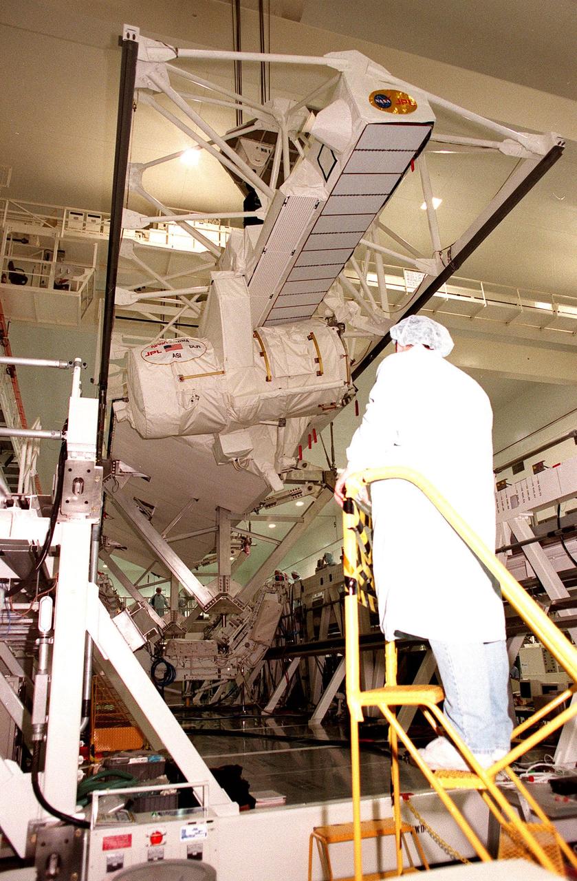Inside the Space Station Processing Facility, workers at each end of a workstand watch as the Shuttle Radar Topography Mission (SRTM) begins its descent onto it. The SRTM, which is the primary payload on mission STS-99, consists of a specially modified radar system that will fly onboard the Space Shuttle during the 11-day mission scheduled for launch in September 1999. The objective of this radar system is to obtain the most complete high-resolution digital topographic database of the Earth. It will gather data that will result in the most accurate and complete topographic map of the Earth's surface that has ever been assembled. SRTM is an international project spearheaded by the National Imagery and Mapping Agency and NASA, with participation of the German Aerospace Center DLR. SRTM will be making use of a technique called radar interferometry, wherein two radar images are taken from slightly different locations. Differences between these images allow for the calculation of surface elevation, or change. To get two radar images taken from different locations, the SRTM hardware will consist of one radar antenna in the shuttle payload bay and a second radar antenna attached to the end of a mast extended 60 meters (195 feet) out from the shuttle