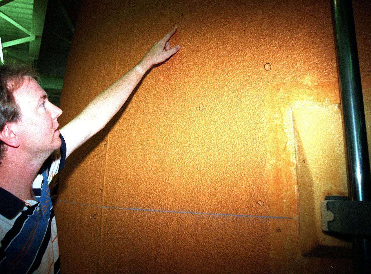 KENNEDY SPACE CENTER, FLA. --  Inside High Bay 1 of the Vehicle Assembly Building (VAB), John Blue, with United Space Alliance, points to one of the divots in the foam insulation on the external tank of Space Shuttle Discovery. About 150 divots were caused by hail during recent storms. The Shuttle was rolled back from Pad 39B to the VAB for repairs because access to all of the damaged areas was not possible at the pad. The work is expected to take two to three days, allowing Discovery to roll back to the pad as early as May 20 for launch of mission STS-96, the 94th launch in the Space Shuttle Program. Liftoff will occur no earlier than May 27. STS-96 is a logistics and resupply mission for the International Space Station, carrying such payloads as a Russian crane, the Strela; a U.S.-built crane; the Spacehab Oceaneering Space System Box (SHOSS), a logistics items carrier; and STARSHINE, a student-shared experiment