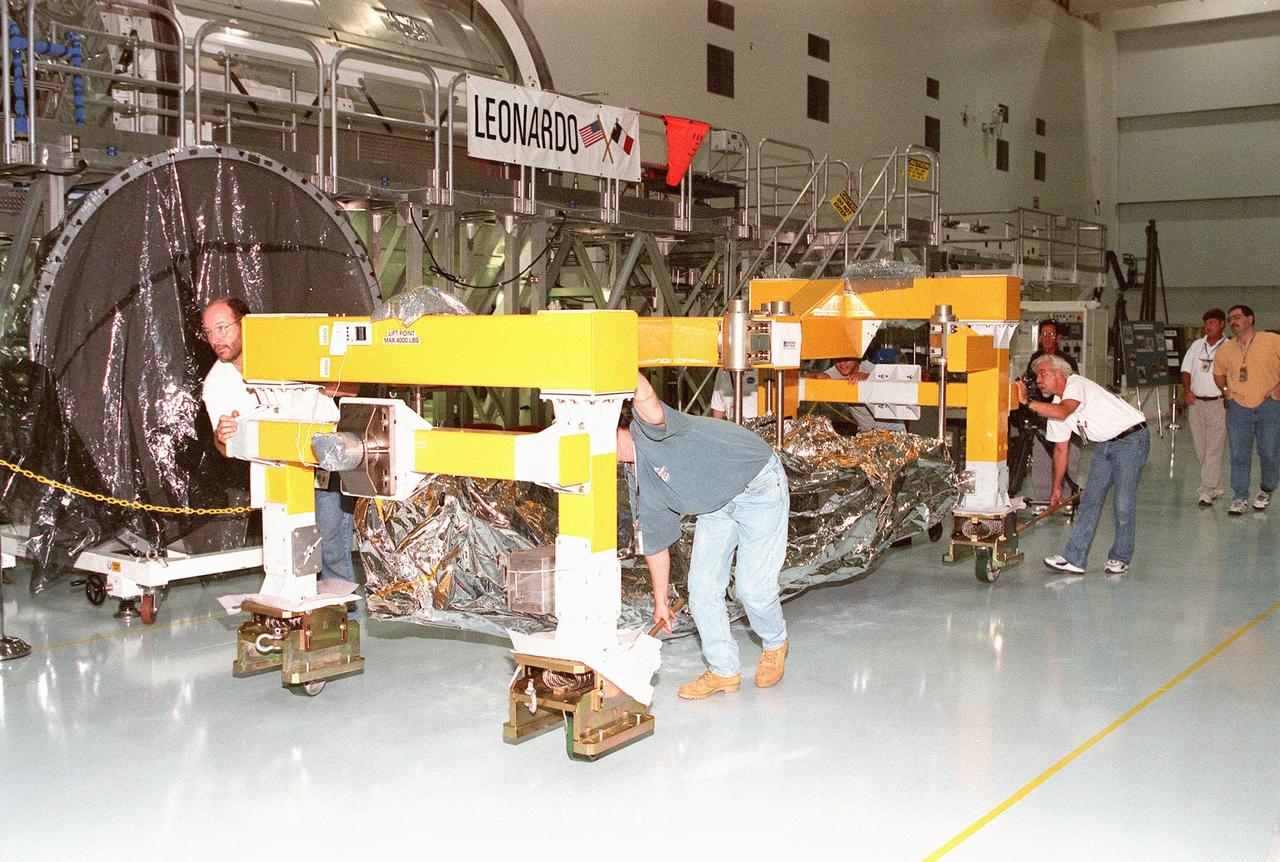 Workers guide a segment of the Canadian Space Agency's (CSA) Space Station Remote Manipulator System (SSRMS) past the Leonardo Multi-Purpose Logistics Module in the Space Station Processing Facility at KSC. The segment joins two others for a campaign of prelaunch processing activities. CSA's first contribution to the International Space Station (ISS), the SSRMS is the primary means of transferring payloads between the orbiter payload bay and the ISS for assembly. The 56-foot-long robotic arm includes two 12-foot booms joined by a hinge. Seven joints on the arm allow highly flexible and precise movement. Latching End Effectors are mounted on each end of the arm for grappling. Video cameras mounted on the booms and end effectors will give astronauts maximum visibility for operations and maintenance tasks on the ISS. The SSRMS is scheduled to be launched aboard Space Shuttle Endeavour on STS-100, currently planned for July 2000