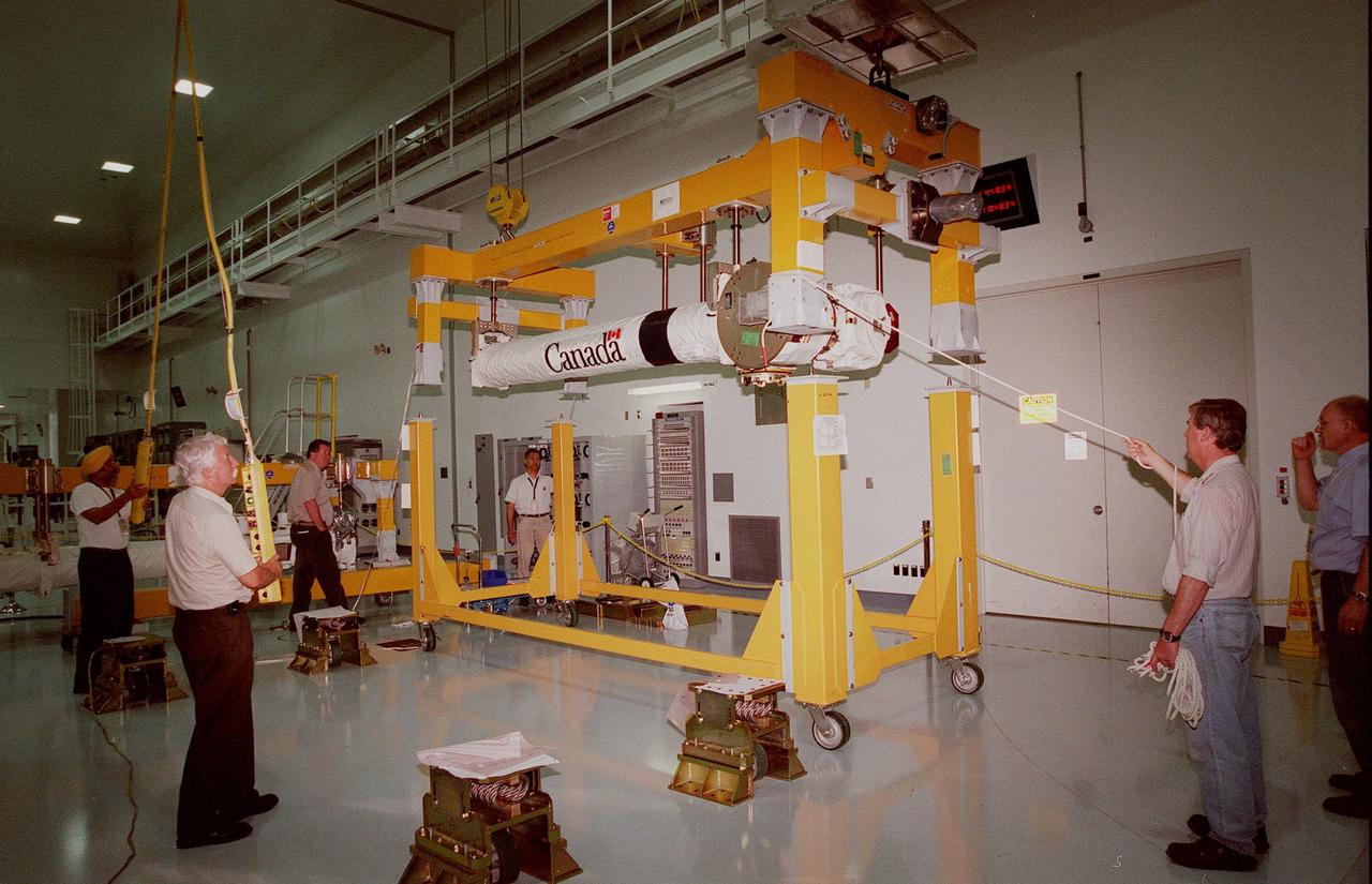 Workers in the in the Space Station Processing Facility move two segments of the Canadian Space Agency's Space Station Remote Manipulator System (SSRMS) to a workstand. CSA's first contribution to the International Space Station (ISS), the SSRMS is the primary means of transferring payloads between the orbiter payload bay and the ISS for assembly. The 56-foot-long robotic arm includes two 12-foot booms joined by a hinge. Seven joints on the arm allow highly flexible and precise movement.. Latching End Effectors are mounted on each end of the arm for grappling. Video cameras mounted on the booms and end effectors will give astronauts maximum visibility for operations and maintenance tasks on the ISS. The SSRMS is at KSC to begin a campaign of prelaunch processing activities. It is scheduled to be launched aboard Space Shuttle Endeavour on mission STS-100, currently planned for July 2000
