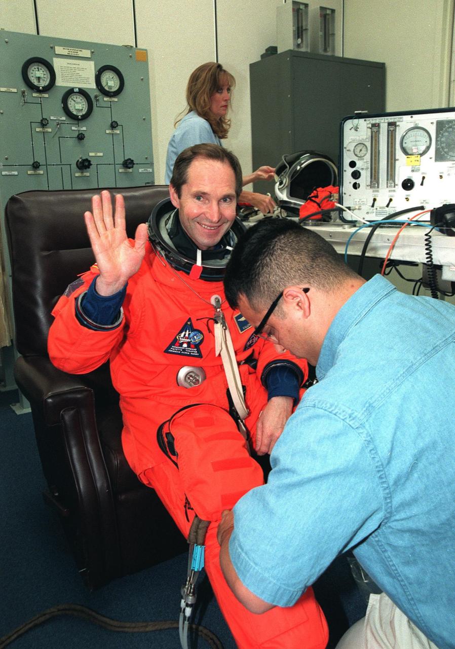 In the Operations and Checkout Building, STS-96 Mission Specialist Valery Ivanovich Tokarev, who represents the Russian Space Agency, waves as he is assisted by a suit technician in donning his launch and entry suit during final launch preparations. STS-96 is a 10-day logistics and resupply mission for the International Space Station, carrying about 4,000 pounds of supplies, to be stored aboard the station for use by future crews, including laptop computers, cameras, tools, spare parts, and clothing. The mission also includes such payloads as a Russian crane, the Strela; a U.S.-built crane; the Spacehab Oceaneering Space System Box (SHOSS), a logistics items carrier; and STARSHINE, a student-involved experiment. It will include a space walk to attach the cranes to the outside of the ISS for use in future construction.. Space Shuttle Discovery is due to launch today at 6:49 a.m. EDT. Landing is expected at the SLF on June 6 about 1:58 a.m. EDT