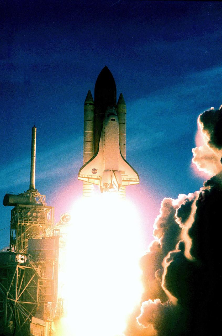 KENNEDY SPACE CENTER, FLA. -- On its perfect launch today, Space Shuttle Discovery's brilliant flames illuminate the tower at left, with the lightning mast on top, and the billows of smoke and steam at right. Liftoff into a gossamer dawn sky for mission STS-96 occurred at 6:49:42 a.m. EDT. The crew of seven begin a 10-day logistics and resupply mission for the International Space Station, carrying about 4,000 pounds of supplies, to be stored aboard the station for use by future crews, including laptop computers, cameras, tools, spare parts, and clothing. The mission also includes such payloads as a Russian crane, the Strela; a U.S.-built crane; the Spacehab Oceaneering Space System Box (SHOSS), a logistics items carrier; and STARSHINE, a student-involved experiment. It will include a space walk to attach the cranes to the outside of the ISS for use in future construction. Landing is expected at the SLF on June 6 about 1:58 a.m. EDT