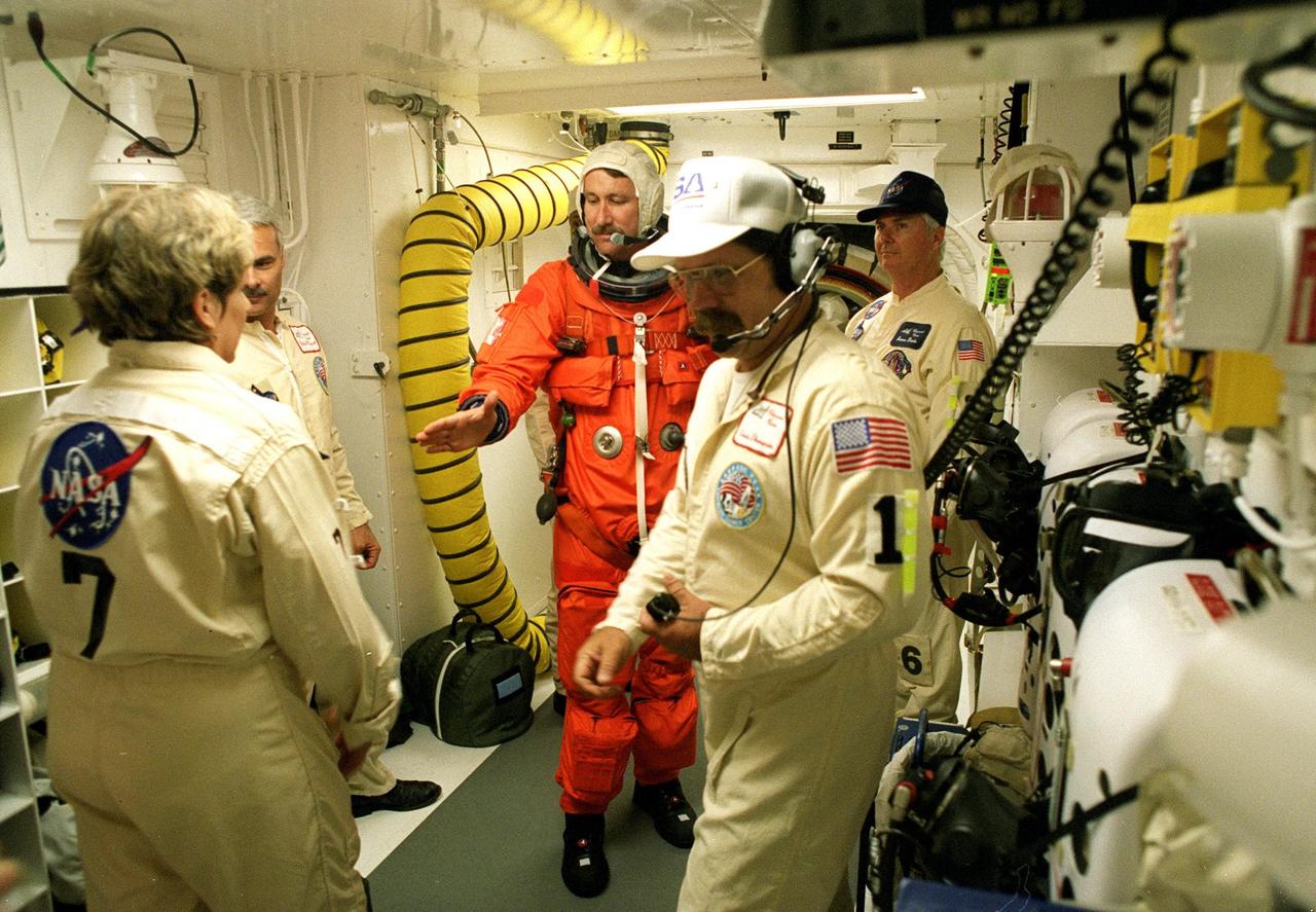 In the white room prior to launch, STS-96 Commander Kent V. Rominger reaches to shake hands with Suit Technician Jean Alexander. The white room is an environmental chamber at the end of the orbiter access arm that provides entry to the orbiter crew compartment. At right are closeout crew members Chief Travis Thompson and Quality Assurance Specialist James Davis; at left is Mechanical Technician Chris Meinert. STS-96 is a 10-day logistics and resupply mission for the International Space Station, carrying about 4,000 pounds of supplies, to be stored aboard the station for use by future crews, including laptop computers, cameras, tools, spare parts, and clothing. The mission also includes such payloads as a Russian crane, the Strela; a U.S.-built crane; the Spacehab Oceaneering Space System Box (SHOSS), a logistics items carrier; and STARSHINE, a student-involved experiment. It will include a space walk to attach the cranes to the outside of the ISS for use in future construction. Space Shuttle Discovery is due to launch today at 6:49 a.m. EDT. Landing is expected at the SLF on June 6 about 1:58 a.m. EDT