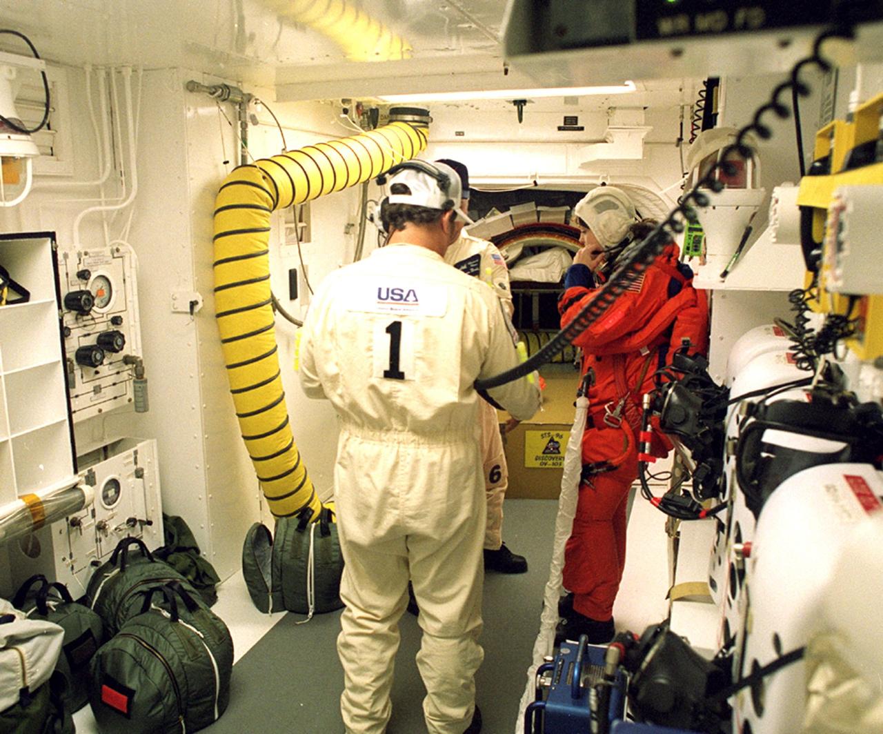 Before entering the orbiter Discovery, STS-96 Mission Specialist Tamara E. Jernigan is checked out in the white room by Closeout Crew Chief Travis Thompson (back to camera) and Quality Assurance Specialist James Davis. The white room is an environmental chamber at the end of the orbiter access arm that provides entry to the orbiter crew compartment. STS-96 is a 10-day logistics and resupply mission for the International Space Station, carrying about 4,000 pounds of supplies, to be stored aboard the station for use by future crews, including laptop computers, cameras, tools, spare parts, and clothing. The mission also includes such payloads as a Russian crane, the Strela; a U.S.-built crane; the Spacehab Oceaneering Space System Box (SHOSS), a logistics items carrier; and STARSHINE, a student-involved experiment. It will include a space walk to attach the cranes to the outside of the ISS for use in future construction. Space Shuttle Discovery is due to launch today at 6:49 a.m. EDT. Landing is expected at the SLF on June 6 about 1:58 a.m. EDT