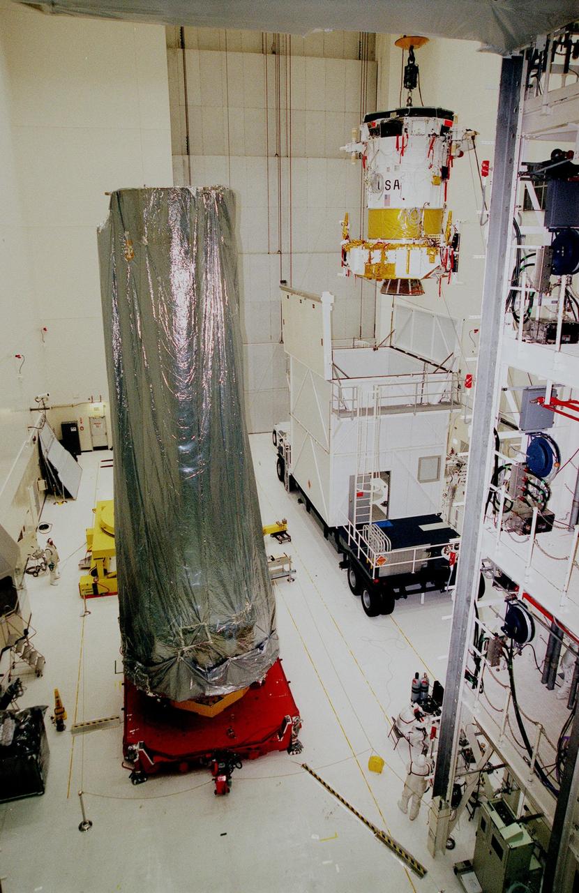 The Inertial Upper Stage (IUS) booster (right) is lifted out of its container after arriving at Kennedy Space Center's Vertical Processing Facility. The IUS will be mated with the Chandra X-ray Observatory (at left) and then undergo testing to validate the IUS/Chandra connections and check the orbiter avionics interfaces. Following that, an end-to-end test (ETE) will be conducted to verify the communications path to Chandra, commanding it as if it were in space. With the world's most powerful X-ray telescope, Chandra will allow scientists from around the world to see previously invisible black holes and high-temperature gas clouds, giving the observatory the potential to rewrite the books on the structure and evolution of our universe. Chandra is scheduled for launch July 22 aboard Space Shuttle Columbia, on mission STS-93