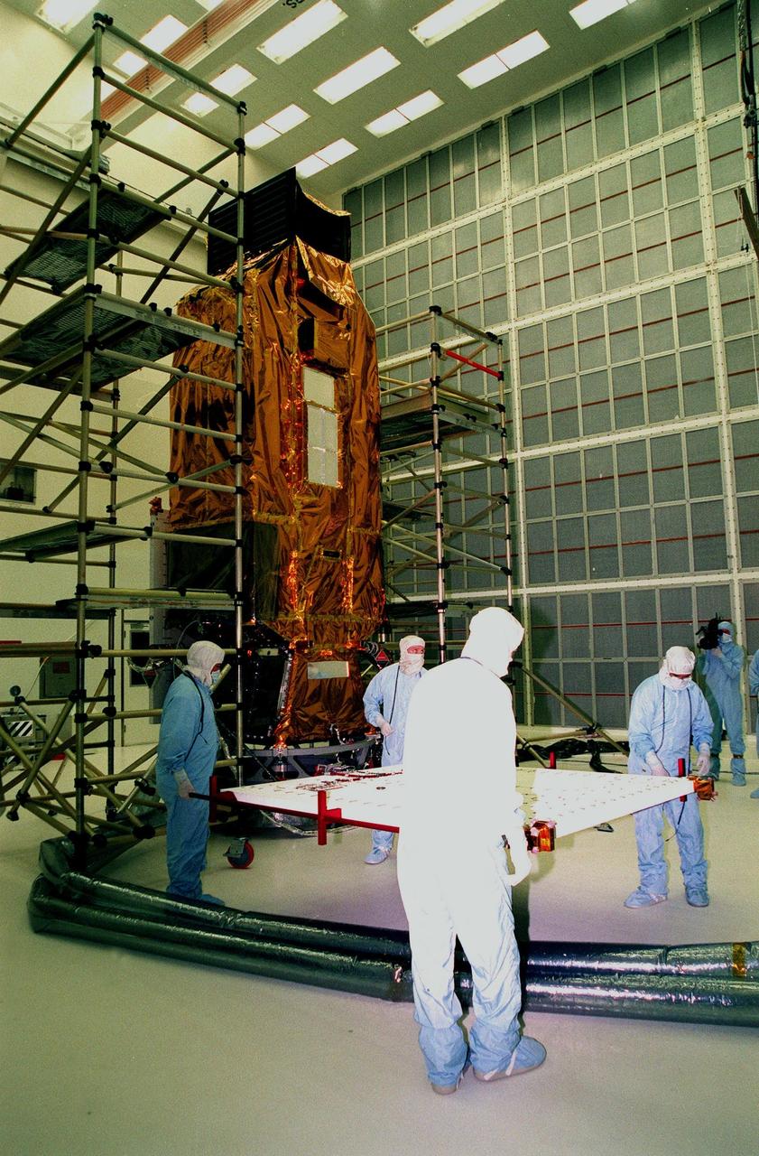 At Hangar AE, Cape Canaveral Air Station (CCAS), workers get ready to move a solar panel to be attached to NASA's Far Ultraviolet Spectroscopic Explorer (FUSE) satellite in the background. FUSE was developed by The Johns Hopkins University under contract to Goddard Space Flight Center, Greenbelt, Md., to investigate the origin and evolution of the lightest elements in the universe hydrogen and deuterium. In addition, the FUSE satellite will examine the forces and process involved in the evolution of the galaxies, stars and planetary systems by investigating light in the far ultraviolet portion of the electromagnetic spectrum. FUSE is targeted for launch June 23 from Launch Pad 17A, CCAS, aboard a Boeing Delta II rocket