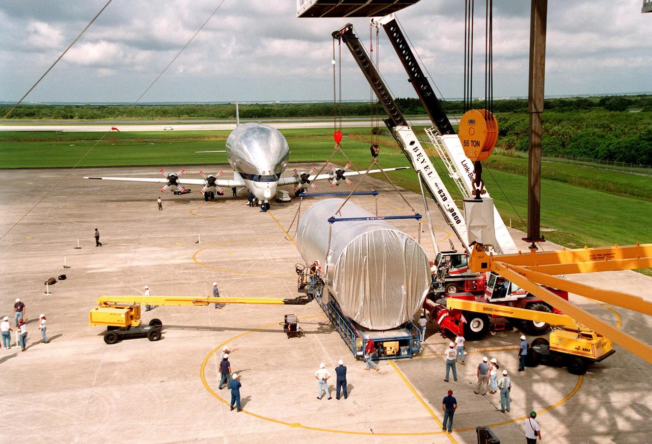 KENNEDY SPACE CENTER, FLA. -- At KSC's Shuttle Landing Facility (SLF), overhead cranes are fitted around the S0 truss segment to move it onto a flatbed trailer which will transfer it to the Operations and Checkout Bldg. for processing. The truss arrived at the SLF aboard the "Super Guppy" aircraft (in the background) from Boeing in Huntington, Calif. During processing, the Canadian Mobile Transporter will be installed on the S0 truss, followed by power distribution system modules, a heat pipe radiator for cooling, computers, and a pair of rate gyroscopes. Four Global Positioning System antennas are already installed. A 44by 15-foot structure weighing 30,800 pounds when fully outfitted and ready for launch, the truss will be at the center of the ISS 10-truss, girderlike structure that will ultimately extend the length of a football field. Eventually the S0 truss will be attached to the U.S. Lab, "Destiny," which is scheduled to be added to the ISS in April 2000. Later, other trusses will be attached to the S0 on-orbit. The S0 truss is scheduled to be launched in the first quarter of 2001 on mission STS-108