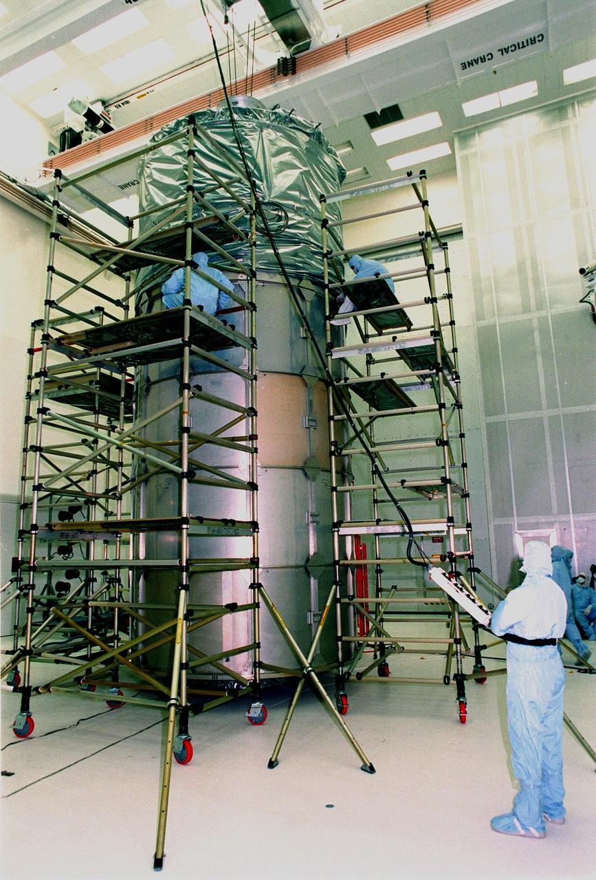 At Hangar AE, Cape Canaveral Air Station (CCAS), workers on scaffolding pull down a weather-proofing cover over the canister surrounding NASA's Far Ultraviolet Spectroscopic Explorer (FUSE) satellite. The satellite will next be moved to Launch Pad 17A, CCAS, for its scheduled launch June 23 aboard a Boeing Delta II rocket. FUSE was developed by The Johns Hopkins University under contract to Goddard Space Flight Center, Greenbelt, Md., to investigate the origin and evolution of the lightest elements in the universe hydrogen and deuterium. In addition, the FUSE satellite will examine the forces and process involved in the evolution of the galaxies, stars and planetary systems by investigating light in the far ultraviolet portion of the electromagnetic spectrum