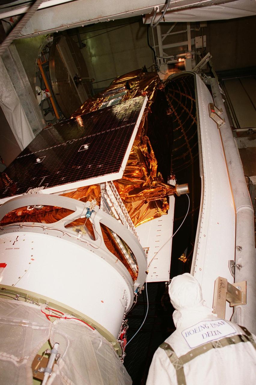 A worker in the launch tower at Launch Pad 17A, Cape Canaveral Air Station, watches as the first segment of the fairing is maneuvered around NASA's Far Ultraviolet Spectroscopic Explorer (FUSE) satellite. The satellite is scheduled for launch June 24 aboard a Boeing Delta II rocket. At the lower left in the photo can be seen a camera installed on the second stage of the rocket to record the separation of the fairing several minutes after launch. FUSE is designed to scour the cosmos for the fossil record of the origins of the universe hydrogen and deuterium. Scientists will use FUSE to study those elements to unlock the secrets of how galaxies evolve and to discover what the Universe was like when it was only a few minutes old