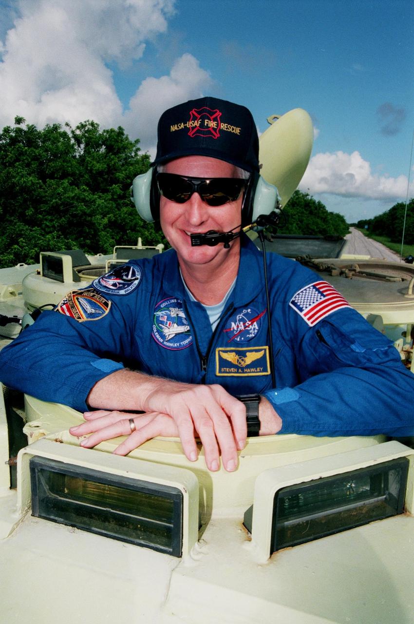 STS-93 Mission Specialist Steven A. Hawley (Ph.D.) smiles for the photographer before climbing into an M-113 armored personnel carrier at the launch pad to take part in emergency egress training. In preparation for their mission, the STS-93 crew are participating in Terminal Countdown Demonstration Test activities that also include a launch-day dress rehearsal culminating with a simulated main engine cut-off. Others in the crew are Commander Eileen M. Collins, Pilot Jeffrey S. Ashby, and Mission Specialists Catherine G. Coleman (Ph.D.) and Michel Tognini of France, who represents the Centre National d'Etudes Spatiales (CNES). Collins is the first woman to serve as a mission commander. The primary mission of STS-93 is the release of the Chandra X-ray Observatory, which will allow scientists from around the world to obtain unprecedented X-ray images of exotic environments in space to help understand the structure and evolution of the universe. Chandra is expected to provide unique and crucial information on the nature of objects ranging from comets in our solar system to quasars at the edge of the observable universe. Since X-rays are absorbed by the Earth's atmosphere, space-based observatories are necessary to study these phenomena and allow scientists to analyze some of the greatest mysteries of the universe. The targeted launch date for STS-93 is no earlier than July 20 at 12:36 a.m. EDT from Launch Pad 39B