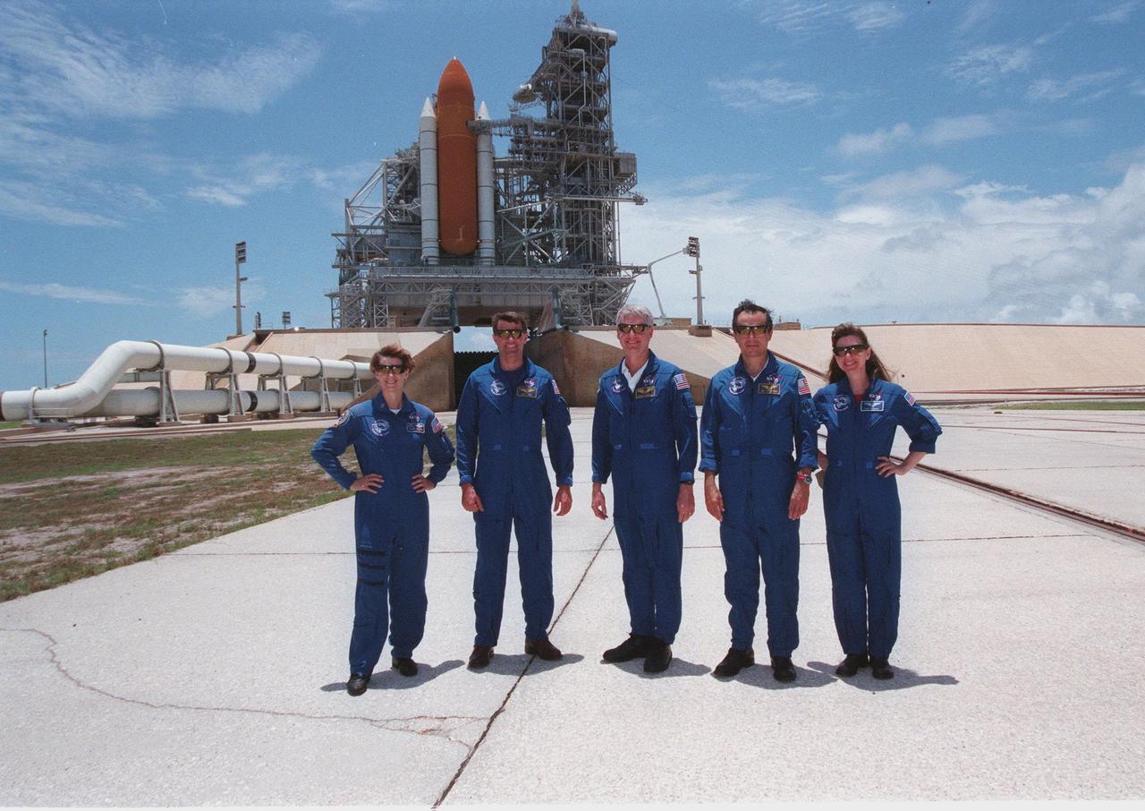 The STS-93 crew poses for a photo on Launch Pad 39B during a break in Terminal Countdown Demonstration Test (TCDT) activities. From left are Commander Eileen M. Collins, Pilot Jeffrey S. Ashby, and Mission Specialists Steven A. Hawley (Ph.D.), Michel Tognini of France, who represents the Centre National d'Etudes Spatiales (CNES), and Catherine G. Coleman (Ph.D.). Collins is the first woman to serve as a Shuttle commander. Behind them is the Space Shuttle Columbia, with only the solid rocket boosters and external tank showing, on the mobile launcher platform. In preparation for their mission, the STS-93 crew members are participating in the TCDT, which familiarizes them with the mission, provides training in emergency exit from the orbiter and launch pad, and includes a launch-day dress rehearsal culminating with a simulated main engine cut-off. The primary mission of STS-93 is the release of the Chandra X-ray Observatory, which will allow scientists from around the world to obtain unprecedented X-ray images of exotic environments in space to help understand the structure and evolution of the universe. The targeted launch date for STS-93 is no earlier than July 20 at 12:36 a.m. EDT from Launch Pad 39B