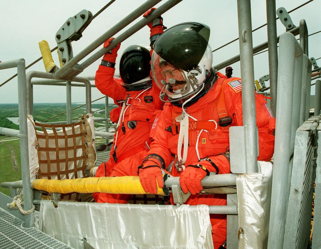 During an emergency egress exercise at the launch pad, Pilot Jeffrey S. Ashby (left) and Commander Eileen M. Collins (right) practice getting into the slidewire basket that is part of an emergency escape route for persons in the Shuttle and on the Rotating Service Structure. The STS-93 crew has been taking part in Terminal Countdown Demonstration Test (TCDT) activities that include the emergency exit training and a launch-day dress rehearsal culminating with a simulated main engine cut-off. Other crew members participating are Mission Specialists Catherine G. Coleman (Ph.D.), Steven A. Hawley (Ph.D.), and Michel Tognini of France, who represents the Centre National d'Etudes Spatiales (CNES). Collins is the first woman to serve as a Shuttle commander. The primary mission of STS-93 is the release of the Chandra X-ray Observatory, which will allow scientists from around the world to obtain unprecedented X-ray images of exotic environments in space to help understand the structure and evolution of the universe. The targeted launch date for STS-93 is no earlier than July 20 at 12:36 a.m. EDT from Launch Pad 39B