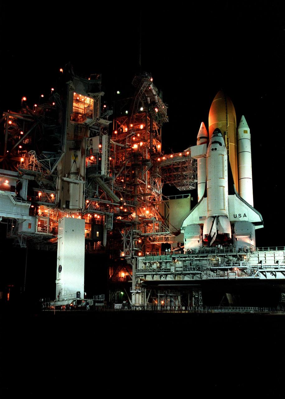 KENNEDY SPACE CENTER, FLA. -- Hours before dawn, the payload canister transporter delivers its cargo (lower left) to Launch Pad 39B, below the Rotating Service Structure (RSS). Inside the canister is the Chandra X-ray Observatory, primary payload on mission STS-93, scheduled to launch no earlier than July 20 aboard Space Shuttle Columbia (right). The canister will be lifted up to the Payload Changeout Room in the RSS where it will be relieved of its cargo. After the RSS rotates to a position behind Columbia, the observatory will then be installed vertically in the orbiter payload bay. The world's most powerful X-ray telescope, Chandra will allow scientists from around the world to see previously invisible black holes and high-temperature gas clouds, giving the observatory the potential to rewrite the books on the structure and evolution of our universe
