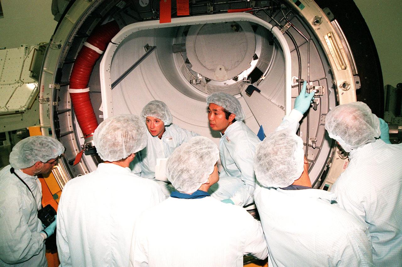 In the Space Station Processing Facility, STS-92 crew members discuss the Pressurized Mating Adapter -3 in the background with workers from Boeing. At the far left is Mission Specialist William Surles "Bill" McArthur Jr.; facing the camera are Pilot Pamela A. Melroy and Mission Specialist Koichi Wakata, who represents the National Space Development Agency of Japan (NASDA). Also participating are other crew members Commander Brian Duffy and Mission Specialists Leroy Chiao (Ph.D.), Peter J.K. "Jeff" Wisoff (Ph.D.), Michael E. Lopez-Alegria and William Surles "Bill" McArthur Jr. The crew are taking part in a Leak Seal Kit Fit Check. The mission payload also includes an integrated truss structure (Z-1 truss). Launch of STS-92 is scheduled for Feb. 24, 2000