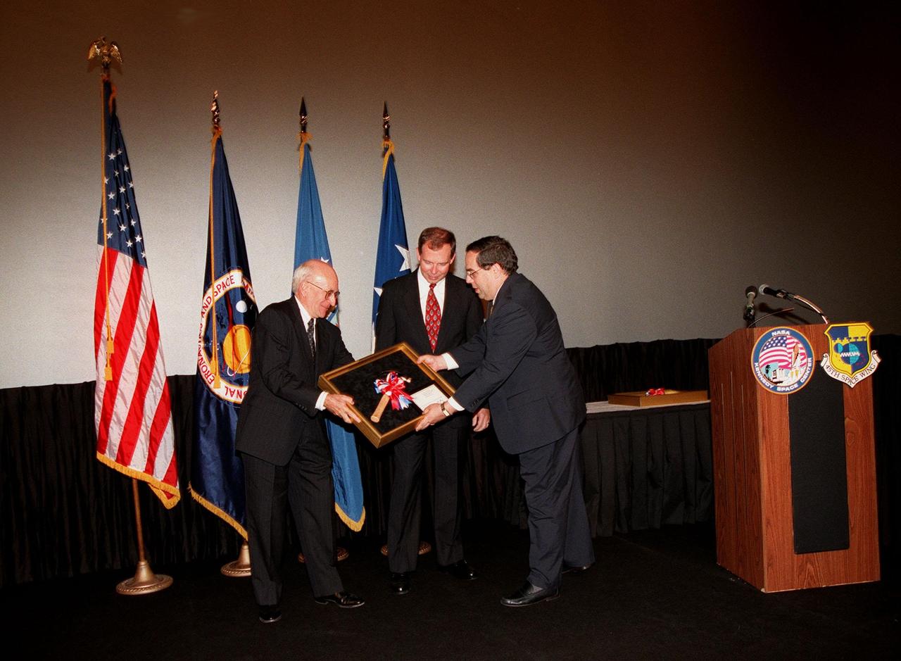 Ed Gormel (left) and Chris Fairey (center) accept the Hammer Award at a special presentation in the IMAX 2 Theater in the Kennedy Space Center Visitor Complex. Presenting the award is Morley Winograd (right), director of the National Partnership for Reinventing Government. The Hammer Award is Vice President Al Gore's special recognition of teams of federal employees who have made significant contributions in support of the principles of the National Partnership for Reinventing Government. This Hammer Award acknowledges the accomplishments of a joint NASA and Air Force team that established the Joint Base Operations and Support Contract (J-BOSC) Source Evaluation Board (SEB). Gormel and Fairey are co-chairs of the SEB. The team developed and implemented the acquisition strategy for establishing a single set of base operations and support service requirements for KSC, Cape Canaveral Air Station and Patrick Air Force Base