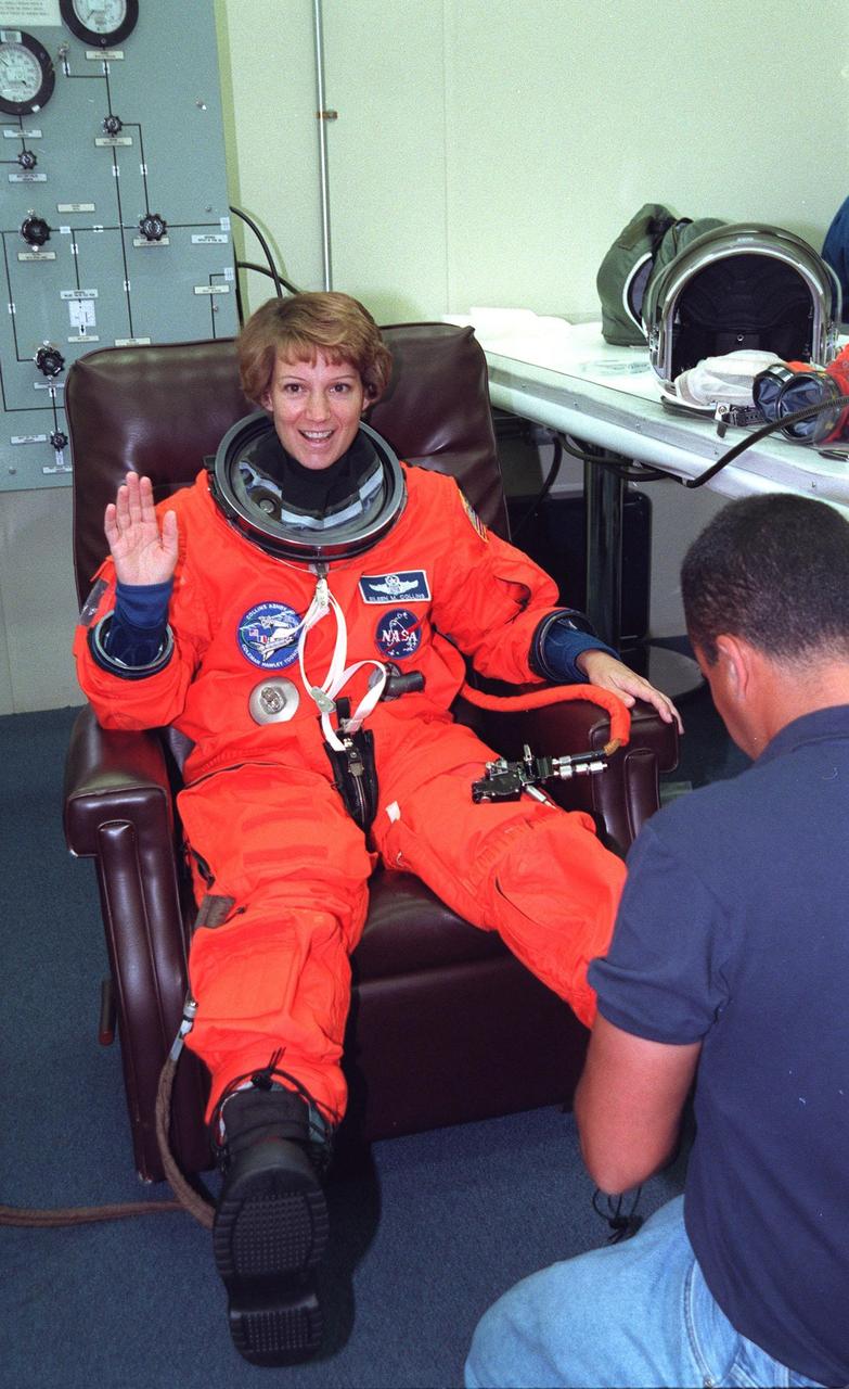 In the Operations and Checkout Building, STS-93 Commander Eileen M. Collins waves while a suit tech adjusts her boot, part of the launch and entry suit, during final launch preparations. STS-93 is a five-day mission primarily to release the Chandra X-ray Observatory, which will allow scientists from around the world to study some of the most distant, powerful and dynamic objects in the universe. The new telescope is 20 to 50 times more sensitive than any previous X-ray telescope and is expected unlock the secrets of supernovae, quasars and black holes. The STS-93 crew numbers five: Commander Collins, Pilot Jeffrey S. Ashby, and Mission Specialists Stephen A. Hawley (Ph.D.), Catherine G. Coleman (Ph.D.) and Michel Tognini of France, with the Centre National d'Etudes Spatiales (CNES). Collins is the first woman to serve as commander of a shuttle mission. STS-93 is scheduled to lift off at 12:36 a.m. EDT July 20. The target landing date is July 24 at 11:30 p.m. EDT