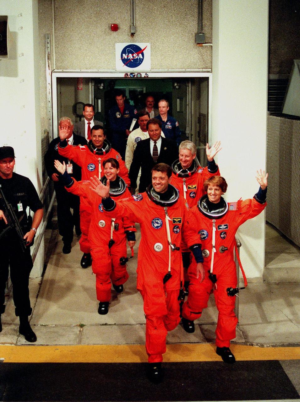 The STS-93 crew wave to onlookers as they walk out of the Operations and Checkout Building enroute to Launch Pad 39-B and liftoff of Space Shuttle Columbia. In their orange launch and entry suits, they are (starting at rear, left to right) Mission Specialists Michel Tognini of France, who represents the Centre National d'Etudes Spatiales (CNES), and Catherine G. Coleman (Ph.D.); Pilot Jeffrey S. Ashby; Mission Specialist Stephen A. Hawley (Ph.D.); and Commander Eileen M. Collins. STS-93 is a five-day mission primarily to release the Chandra X-ray Observatory, which will allow scientists from around the world to study some of the most distant, powerful and dynamic objects in the universe. The new telescope is 20 to 50 times more sensitive than any previous X-ray telescope and is expected unlock the secrets of supernovae, quasars and black holes. Collins is the first woman to serve as commander of a Shuttle mission. STS-93 is scheduled to lift off at 12:36 a.m. EDT July 20. The target landing date is July 24 at 11:31 p.m. EDT