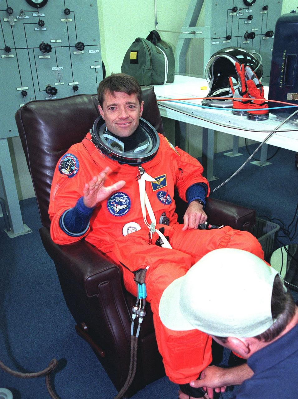 In the Operations and Checkout Building during final launch preparations for the second time, STS-93 Pilot Jeffrey S. Ashby waves after donning his launch and entry suit while a suit tech adjusts his boot. After Space Shuttle Columbia's July 20 launch attempt was scrubbed at the T-7 second mark in the countdown, the launch was rescheduled for Thursday, July 22, at 12:28 a.m. EDT. The target landing date is July 26, 1999, at 11:24 p.m. EDT. STS-93 is a five-day mission primarily to release the Chandra X-ray Observatory, which will allow scientists from around the world to study some of the most distant, powerful and dynamic objects in the universe. The new telescope is 20 to 50 times more sensitive than any previous X-ray telescope and is expected unlock the secrets of supernovae, quasars and black holes. The STS-93 crew numbers five: Commander Eileen M. Collins, Ashby, and Mission Specialists Stephen A. Hawley (Ph.D.), Catherine G. Coleman (Ph.D.) and Michel Tognini of France, with the Centre National d'Etudes Spatiales (CNES). Collins is the first woman to serve as commander of a shuttle mission