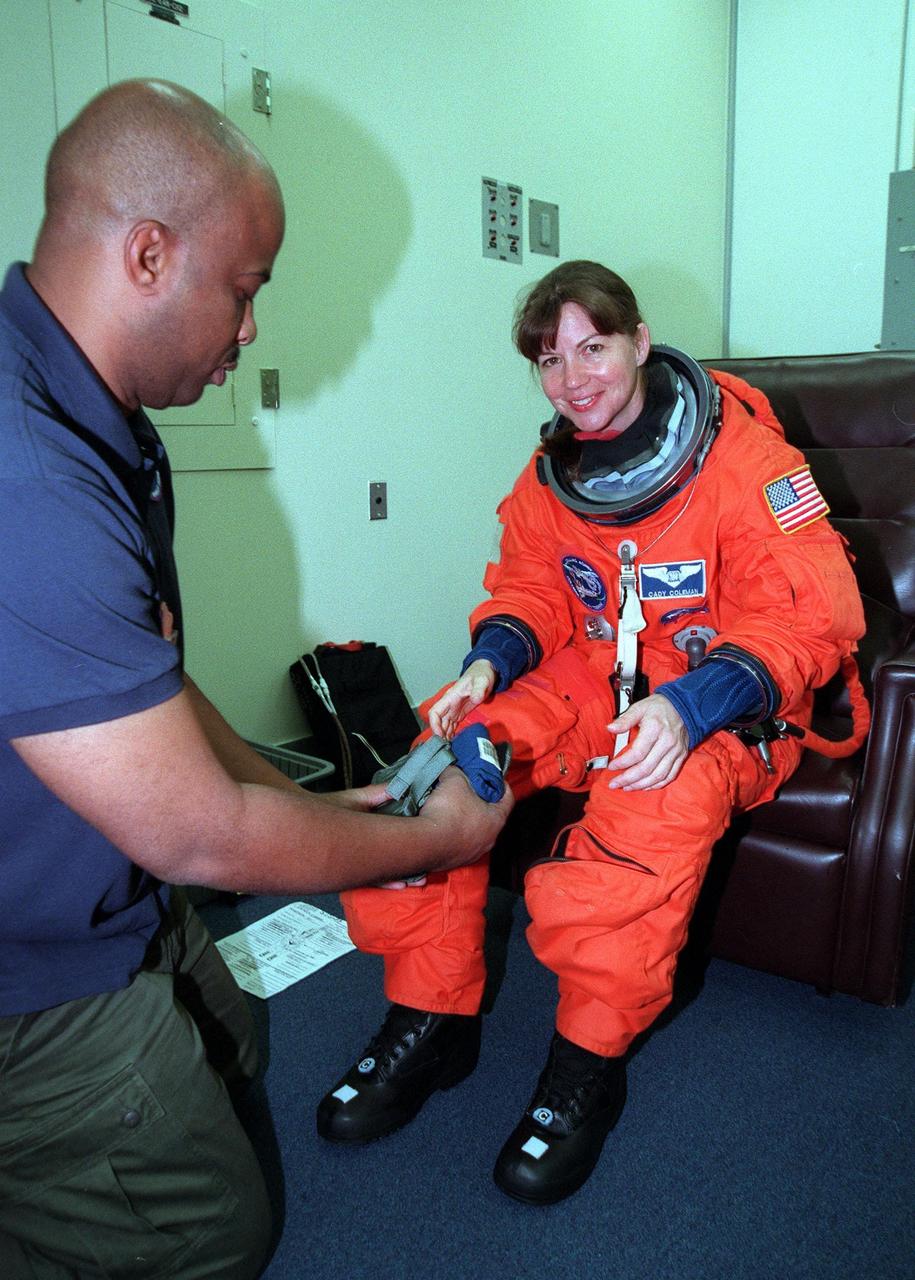 During final launch preparations in the Operations and Checkout Building, STS-93 Mission Specialist Catherine G. Coleman (Ph.D.) gets help with her launch and entry suit from a suit tech. After Space Shuttle Columbia's July 20 launch attempt was scrubbed at the T-7 second mark in the countdown, the launch was rescheduled for Thursday, July 22, at 12:28 a.m. EDT. The target landing date is July 26, 1999, at 11:24 p.m. EDT. STS-93 is a five-day mission primarily to release the Chandra X-ray Observatory, which will allow scientists from around the world to study some of the most distant, powerful and dynamic objects in the universe. The new telescope is 20 to 50 times more sensitive than any previous X-ray telescope and is expected unlock the secrets of supernovae, quasars and black holes. The STS-93 crew numbers five: Commander Eileen M. Collins, Pilot Jeffrey S. Ashby, and Mission Specialists Stephen A. Hawley (Ph.D.), Coleman and Michel Tognini of France, who represents the Centre National d'Etudes Spatiales (CNES). Collins is the first woman to serve as commander of a shuttle mission