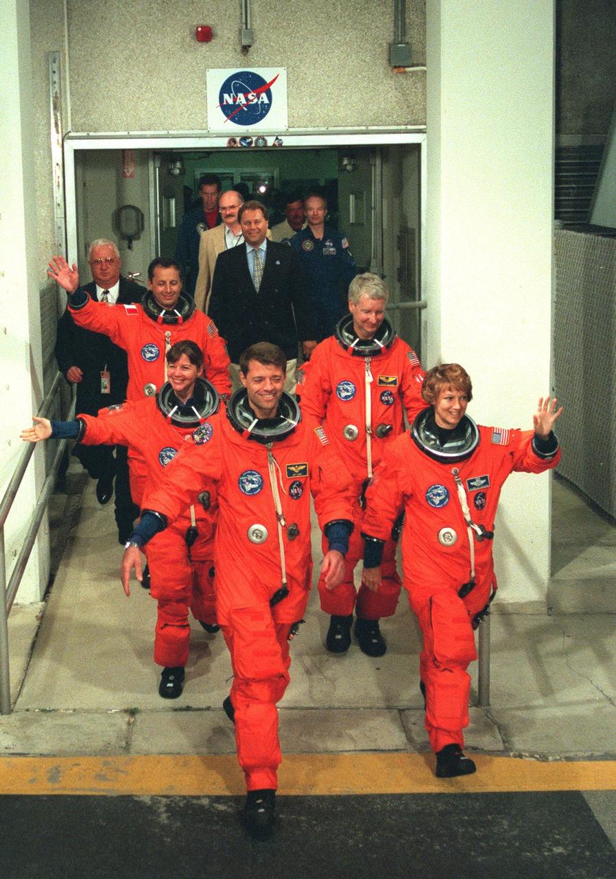 The STS-93 crew wave to onlookers as they walk out of the Operations and Checkout Building for the second time enroute to Launch Pad 39-B and liftoff of Space Shuttle Columbia. After Space Shuttle Columbia's July 20 launch attempt was scrubbed at the T-7 second mark in the countdown, the launch was rescheduled for Thursday, July 22, at 12:28 a.m. EDT. The target landing date is July 26, 1999, at 11:24 p.m. EDT. In their orange launch and entry suits, they are (starting at rear, left to right) Mission Specialists Michel Tognini of France, who represents the Centre National d'Etudes Spatiales (CNES), and Catherine G. Coleman (Ph.D.); Pilot Jeffrey S. Ashby; Mission Specialist Steven A. Hawley (Ph.D.); and Commander Eileen M. Collins. STS-93 is a five-day mission primarily to release the Chandra X-ray Observatory, which will allow scientists from around the world to study some of the most distant, powerful and dynamic objects in the universe. The new telescope is 20 to 50 times more sensitive than any previous X-ray telescope and is expected unlock the secrets of supernovae, quasars and black holes. Collins is the first woman to serve as commander of a Shuttle mission