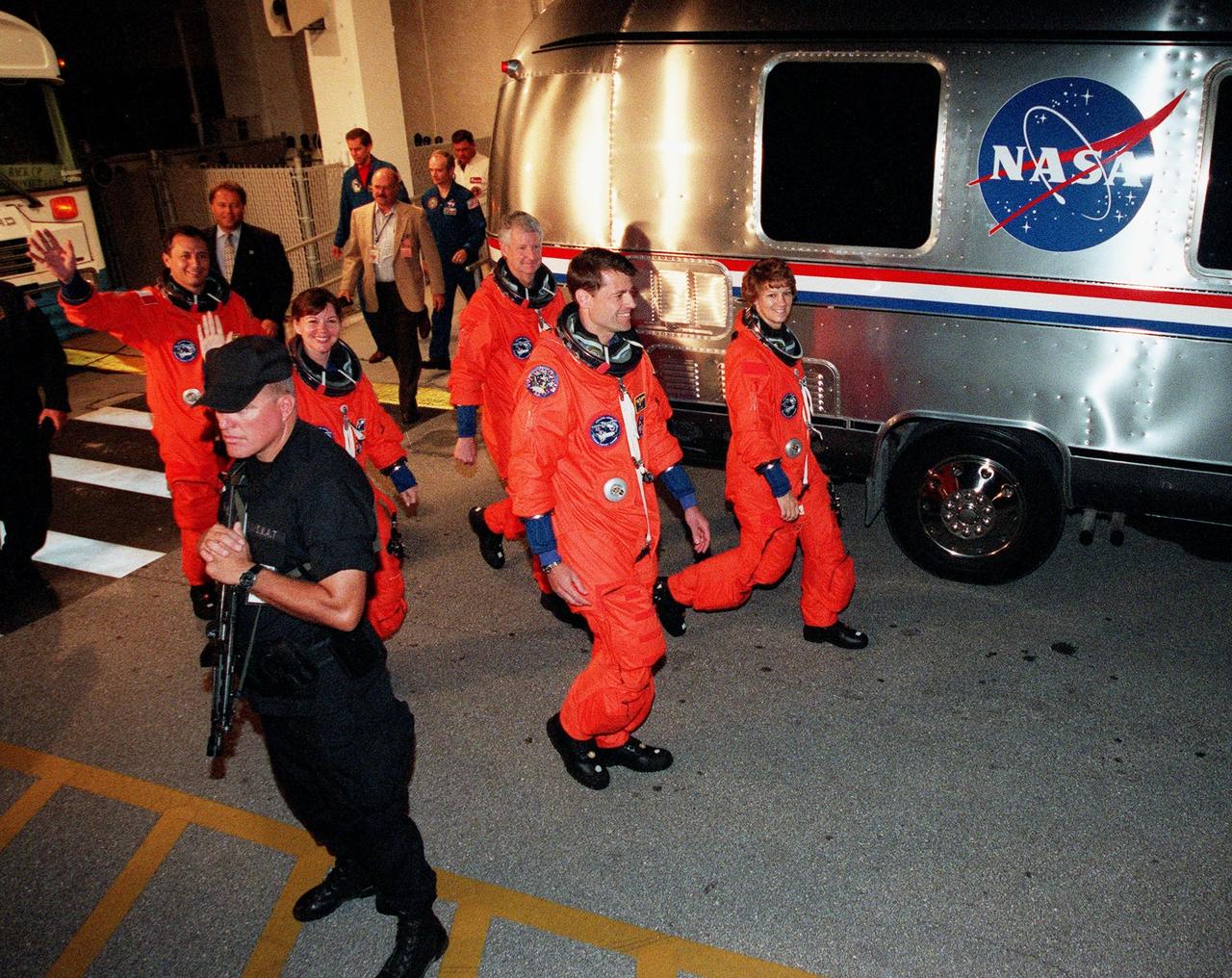 Flanked by security, the STS-93 crew wave to onlookers as they head for the "Astrovan" a second time to take them to Launch Pad 39-B and liftoff of Space Shuttle Columbia. After the July 20 launch attempt was scrubbed at the T-7 second mark in the countdown, the launch was rescheduled for Thursday, July 22, at 12:28 a.m. EDT. The target landing date is July 26, 1999, at 11:24 p.m. EDT. In their orange launch and entry suits, they are (starting at rear, left to right) Mission Specialists Michel Tognini of France, who represents the Centre National d'Etudes Spatiales (CNES), Catherine G. Coleman (Ph.D.), and Steven A. Hawley (Ph.D.); Pilot Jeffrey S. Ashby; and Commander Eileen M. Collins. STS-93 is a five-day mission primarily to release the Chandra X-ray Observatory, which will allow scientists from around the world to study some of the most distant, powerful and dynamic objects in the universe. The new telescope is 20 to 50 times more sensitive than any previous X-ray telescope and is expected unlock the secrets of supernovae, quasars and black holes. Collins is the first woman to serve as commander of a Shuttle mission