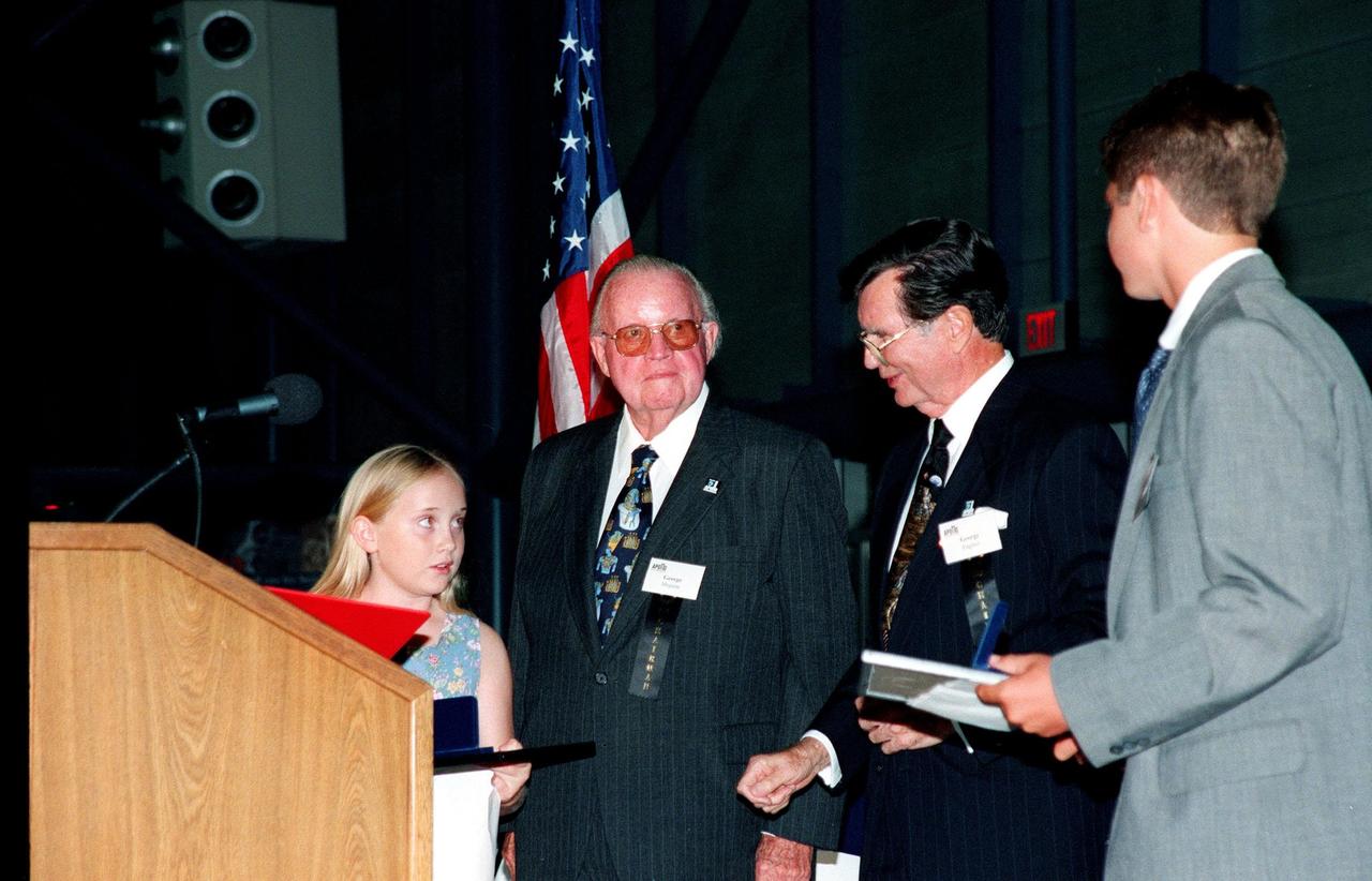 KENNEDY SPACE CENTER, FLA. -- At the Apollo/Saturn V Center, George Meguiar (center left) and George English (center right) present scholarships to two students who entered an essay contest in conjunction with the 30th Anniversary of Apollo 11. The winners shown are Kyla Davis Horn, of Cocoa Beach, and Kyle Rukaczewski, of Satellite Beach. A third winner, Jason Gagnon, of Viera, was unable to attend. Meguiar and English head the Apollo 11 Commemoration Association which sponsored the contest in conjunction with Florida Today newspaper. The presentation was made at the Apollo/Saturn V Center during an anniversary banquet that honored all the people who made the Apollo Program possible. Special guests included former Apollo astronauts Neil Armstrong, Edwin "Buzz" Aldrin, Gene Cernan and Walt Cunningham, who shared their experiences with the audience