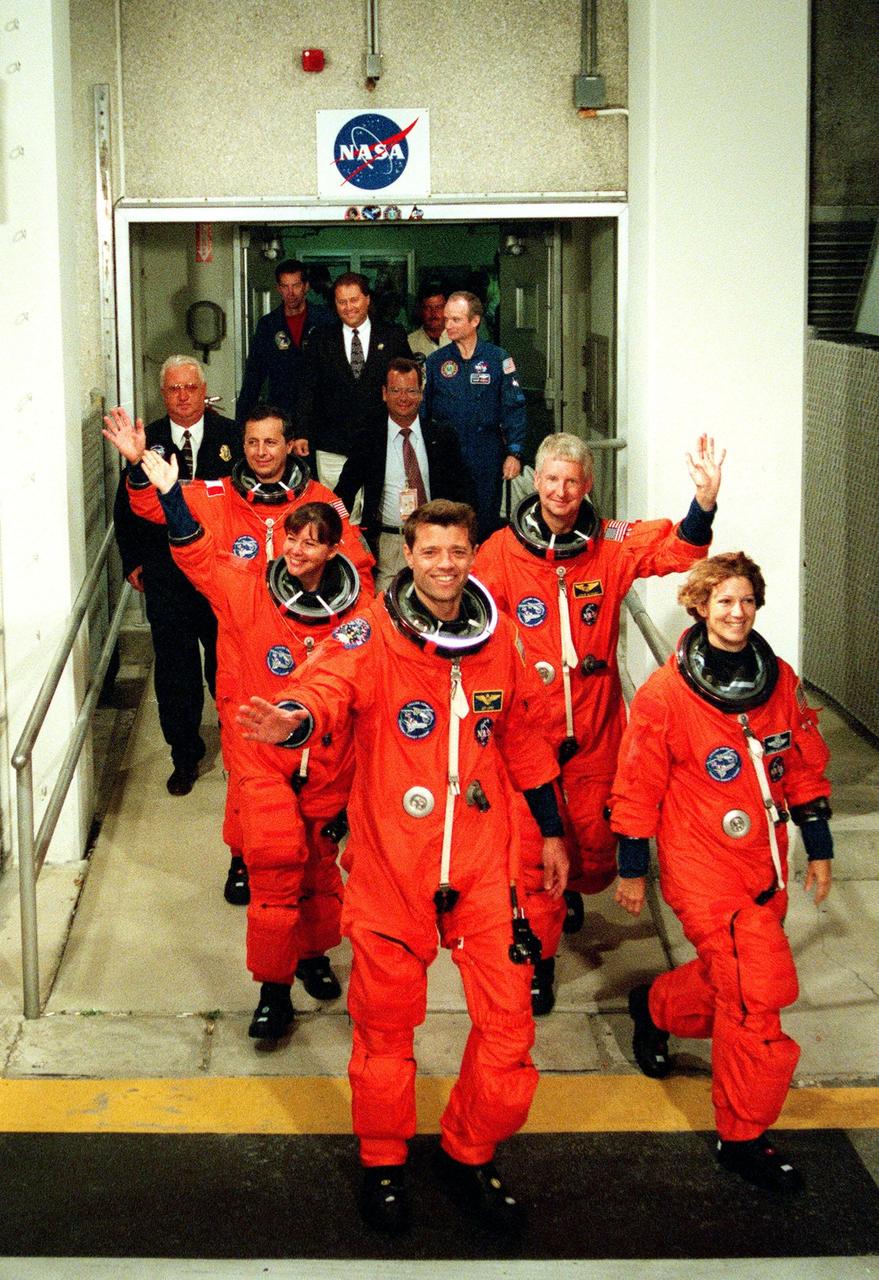 The STS-93 crew wave and smile at onlookers as they walk out of the Operations and Checkout Building for the third time enroute to Launch Pad 39-B and liftoff of Space Shuttle Columbia. After Space Shuttle Columbia's July 20 and 22 launch attempts were scrubbed, the launch was again rescheduled for Friday, July 23, at 12:24 a.m. EDT. The target landing date is July 27, 1999, at 11:20 p.m. EDT. In their orange launch and entry suits, they are (starting at rear, left to right) Mission Specialists Michel Tognini of France, who represents the Centre National d'Etudes Spatiales (CNES), and Catherine G. Coleman (Ph.D.); Pilot Jeffrey S. Ashby; Mission Specialist Steven A. Hawley (Ph.D.); and Commander Eileen M. Collins. STS-93 is a five-day mission primarily to release the Chandra X-ray Observatory, which will allow scientists from around the world to study some of the most distant, powerful and dynamic objects in the universe. Collins is the first woman to serve as commander of a Shuttle mission