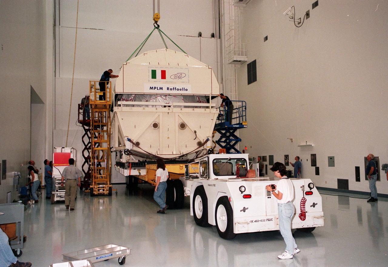 KENNEDY SPACE CENTER, FLA. -- Inside a high bay of the Space Station Processing Facility (SSPF), workers begin removing the shipping canister from around the Multi-Purpose Logistics Module (MPLM) called Raffaello. After transfer to a workstand, the MPLM will undergo testing, joining the first Italian-built MPLM, Leonardo, in the SSPF. One of Italy's major contributions to the ISS program, the MPLM is a reusable logistics carrier and the primary delivery system used to resupply and return station cargo requiring a pressurized environment. Weighing nearly 4.5 tons, the Raffaello measures 21 feet long and 15 feet in diameter. Raffaello is scheduled to be launched on mission STS-100 July 27, 2000