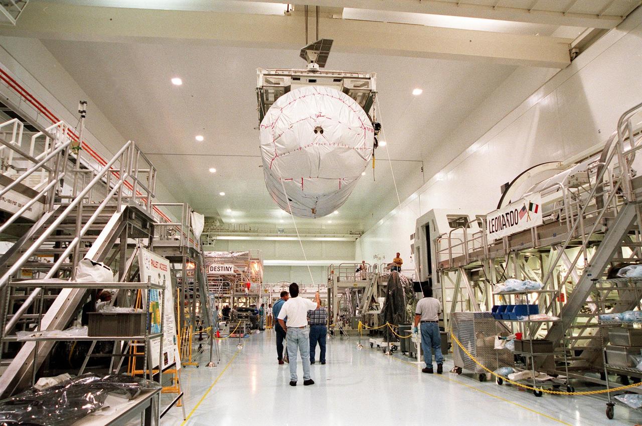 KENNEDY SPACE CENTER, FLA. -- Inside a high bay in the Space Station Processing Facility (SSPF), workers on the floor oversee the transfer of the Multi-Purpose Logistics Module (MPLM) called Raffaello to a workstand where it will undergo testing. Sharing the space in the SSPF is the first Italian-built MPLM, Leonardo, seen at right, and the U.S. Lab, Destiny, in the background. One of Italy's major contributions to the ISS program, the MPLM is a reusable logistics carrier and the primary delivery system used to resupply and return station cargo requiring a pressurized environment. Weighing nearly 4.5 tons, the Raffaello measures 21 feet long and 15 feet in diameter. Raffaello is scheduled to be launched on mission STS-100 July 27, 2000