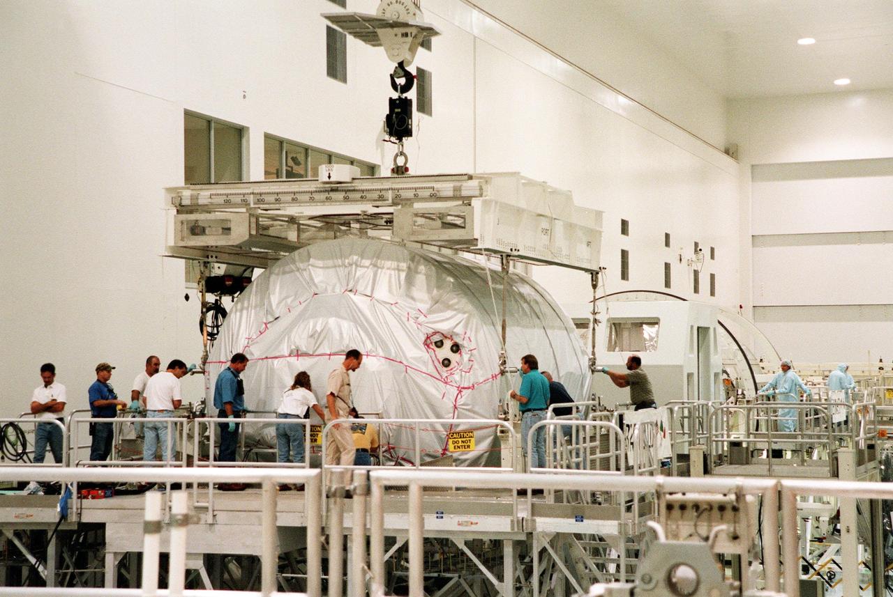 KENNEDY SPACE CENTER, FLA. -- Workers oversee the placement of the Multi-Purpose Logistics Module (MPLM) called Raffaello as a crane lowers it onto a workstand in the Space Station Processing Facility (SSPF). One of Italy's major contributions to the ISS program, the MPLM is a reusable logistics carrier and the primary delivery system used to resupply and return station cargo requiring a pressurized environment. Weighing nearly 4.5 tons, the Raffaello measures 21 feet long and 15 feet in diameter. Raffaello will undergo testing. joining the first Italian-built MPLM, Leonardo, also in the SSPF. Raffaello is scheduled to be launched on mission STS-100 on July 27, 2000