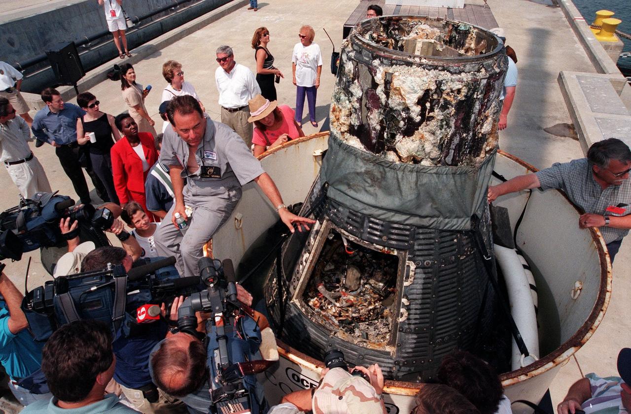 KENNEDY SPACE CENTER, FLA. -- Retrieved from the ocean floor three miles deep, the Liberty Bell 7 Project Mercury capsule is revealed to photographers and the media in Port Canaveral, Fla.  The capsule was found and raised by Curt Newport (left), leading an expedition sponsored by the Discovery Channel.  After its successful 16-minute suborbital flight on July 21, 1961, the Liberty Bell 7, with astronaut Virgil "Gus" Grissom aboard, splashed down in the Atlantic Ocean.  A prematurely jettisoned hatch caused the capsule to flood and a Marine rescue helicopter was unable to lift it.  It quickly sank to a three-mile depth.  Grissom was rescued but his spacecraft remained lost on the ocean floor, until now. An underwater salvage expert, Newport located the capsule through modern technology, and after one abortive attempt, successfully raised it and brought it to Port Canaveral. The recovery of Liberty Bell 7 fulfilled a 14-year dream for the expedition leader.  The capsule is being moved to the Kansas Cosmosphere and Space Center in Hutchinson, Kansas,  where it will be restored for eventual public display. Newport has also been involved in salvage operations of the Space Shuttle Challenger and TWA Flight 800 that crashed off the coast of Long Island, N.Y