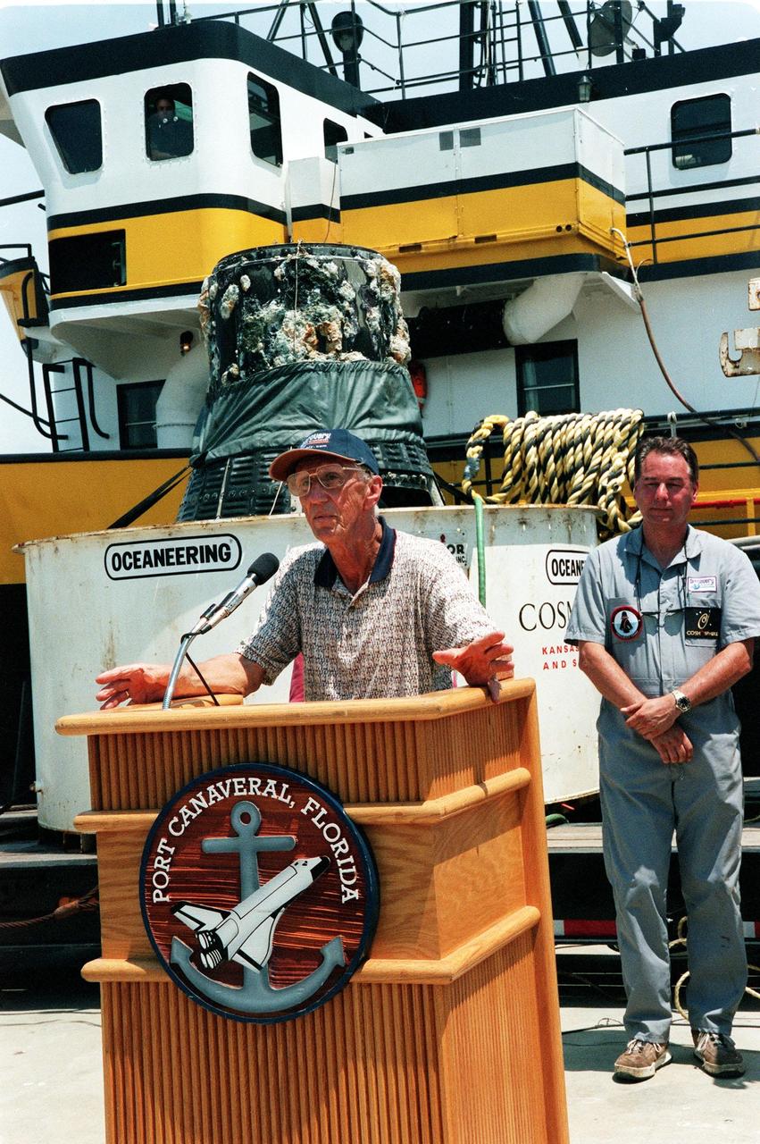 KENNEDY SPACE CENTER, FLA. -- Gunther Wendt takes a turn at the podium after viewing the recovered Liberty Bell 7 Project Mercury capsule, seen in the background.  At right is Curt Newport who led the expedition to find and retrieve the capsule.  The expedition was sponsored by the Discovery Channel.   Wendt worked on the Liberty Bell 7 before its launch July 21, 1961. After its successful 16-minute suborbital flight, the Liberty Bell 7, with astronaut Virgil "Gus" Grissom aboard, splashed down in the Atlantic Ocean.  A prematurely jettisoned hatch caused the capsule to flood and a Marine rescue helicopter was unable to lift it.  It quickly sank to a three-mile depth.  Grissom was rescued but his spacecraft remained lost on the ocean floor, until now. An underwater salvage expert, Newport located the capsule through modern technology, and after one abortive attempt, successfully raised it and brought it to Port Canaveral. The recovery of Liberty Bell 7 fulfilled a 14-year dream for the expedition leader.  The capsule is being moved to the Kansas Cosmosphere and Space Center in Hutchinson, Kansas,  where it will be restored for eventual public display. Newport has also been involved in salvage operations of the Space Shuttle Challenger and TWA Flight 800 that crashed off the coast of Long Island, N.Y